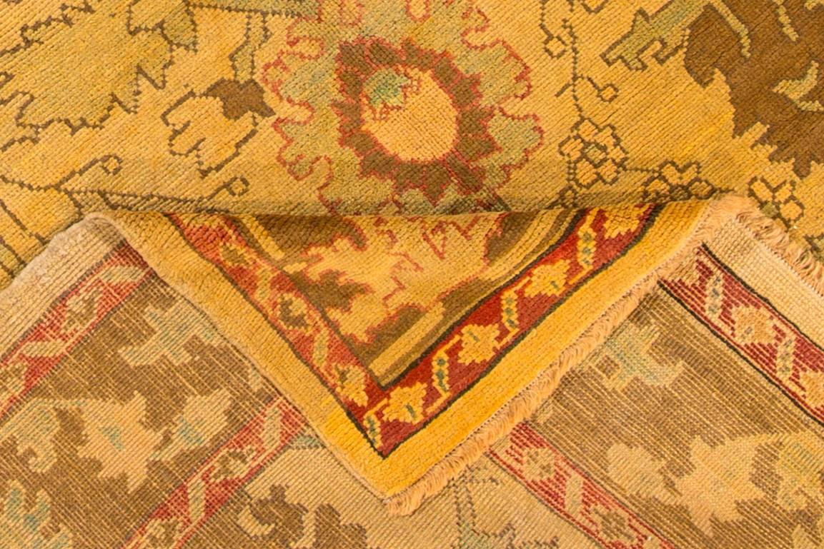 A hand-knotted vintage Oushak-style rug with a floral design on a beige field. Accents of red, green and brown throughout the piece. The size of this piece is 7.11x10.09