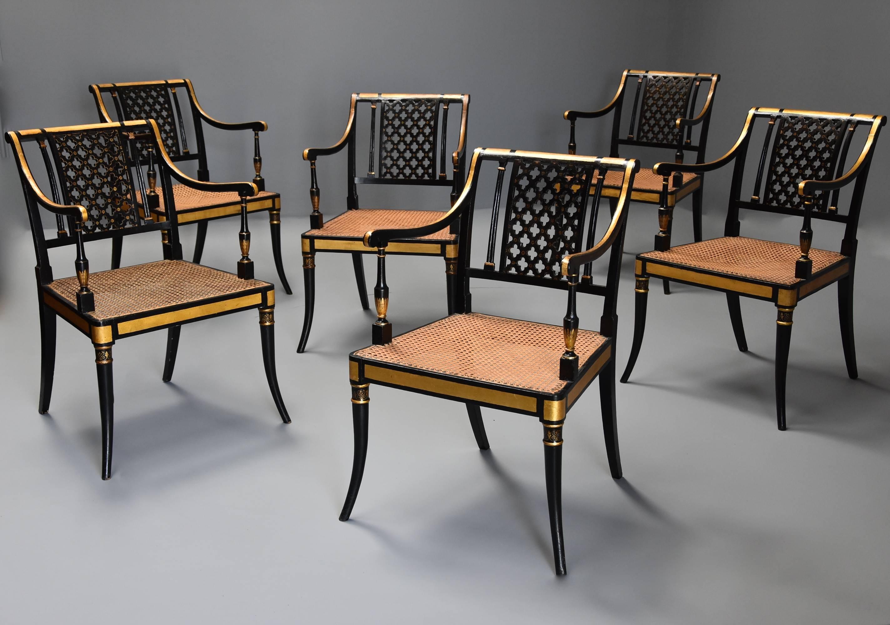 A highly decorative set of six Regency open armchairs with black painted and gilt finish.

This set of chairs each consist of a rounded top rail leading down to a central pierced quatrefoil back splat with painted floral decoration with reeded