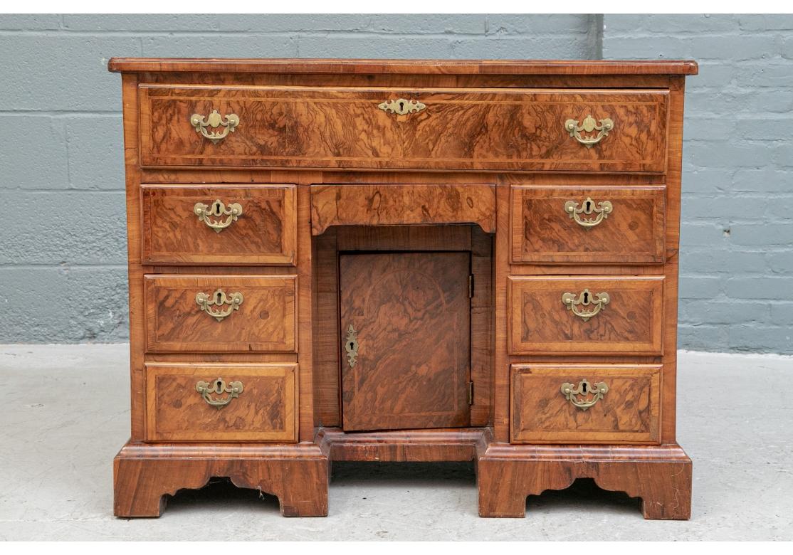 A diminutive size in figured wood with thin banding on top and banded drawers, The frieze with pull down secretary with tooled leather topped writing surface, drawers and a cubby hole. The case with three drawers on each side, all with fine brass