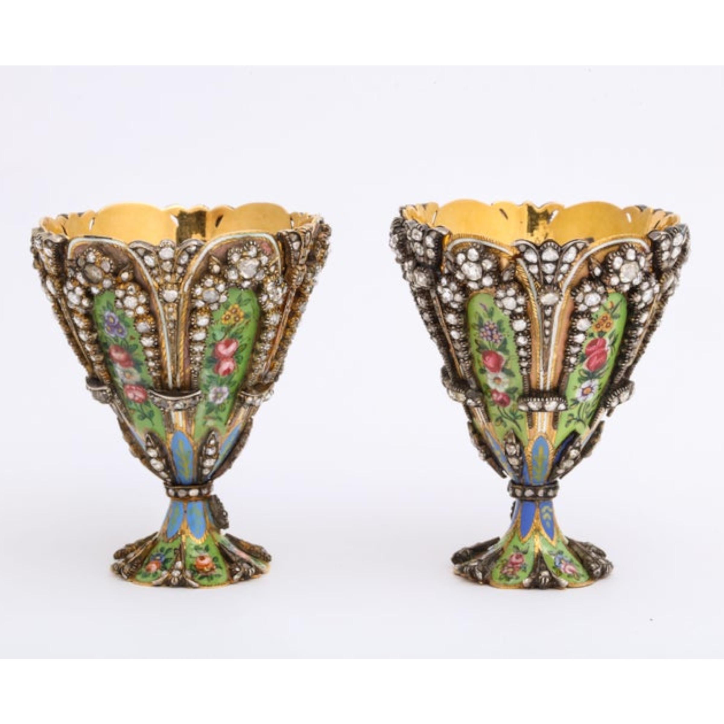 A highly important museum quality pair of diamond and enamel Zarfs.

Each Zarf with a scalloped rim and spreading foot, the sides set with colorful green and pink enamel plaques depicting flower heads and foliage. The stem and the base is a