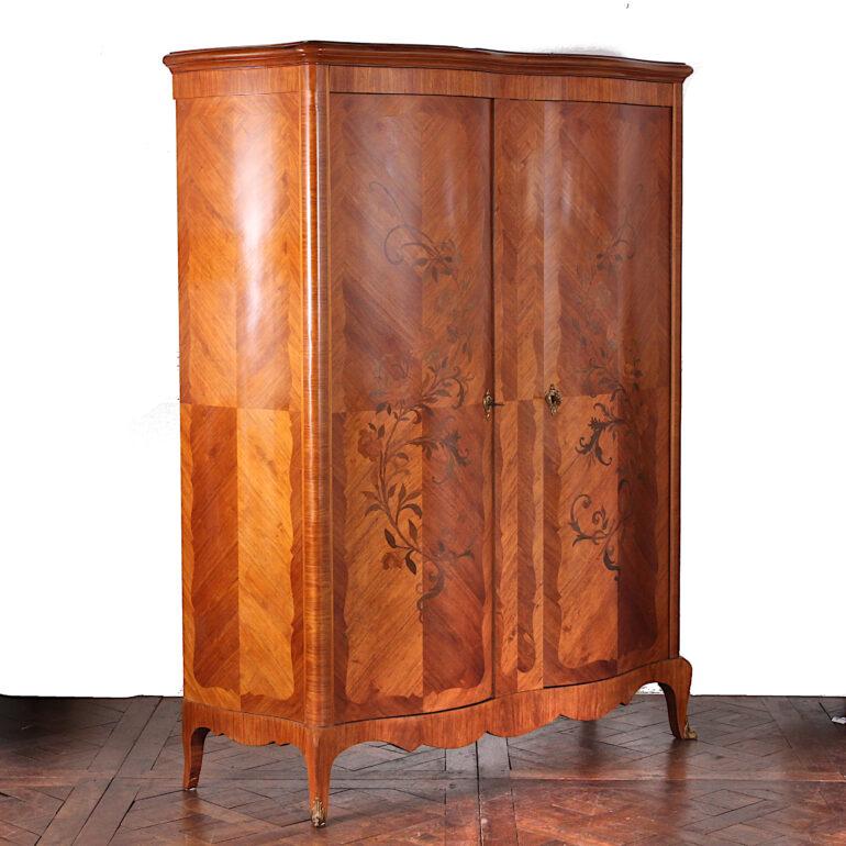 A pretty French serpentine two-door armoire with book-matched kingwood veneer and dramatic inlaid floral marquetry to the doors. The interior is two sections, both with adjustable shelves. C. 1930.



