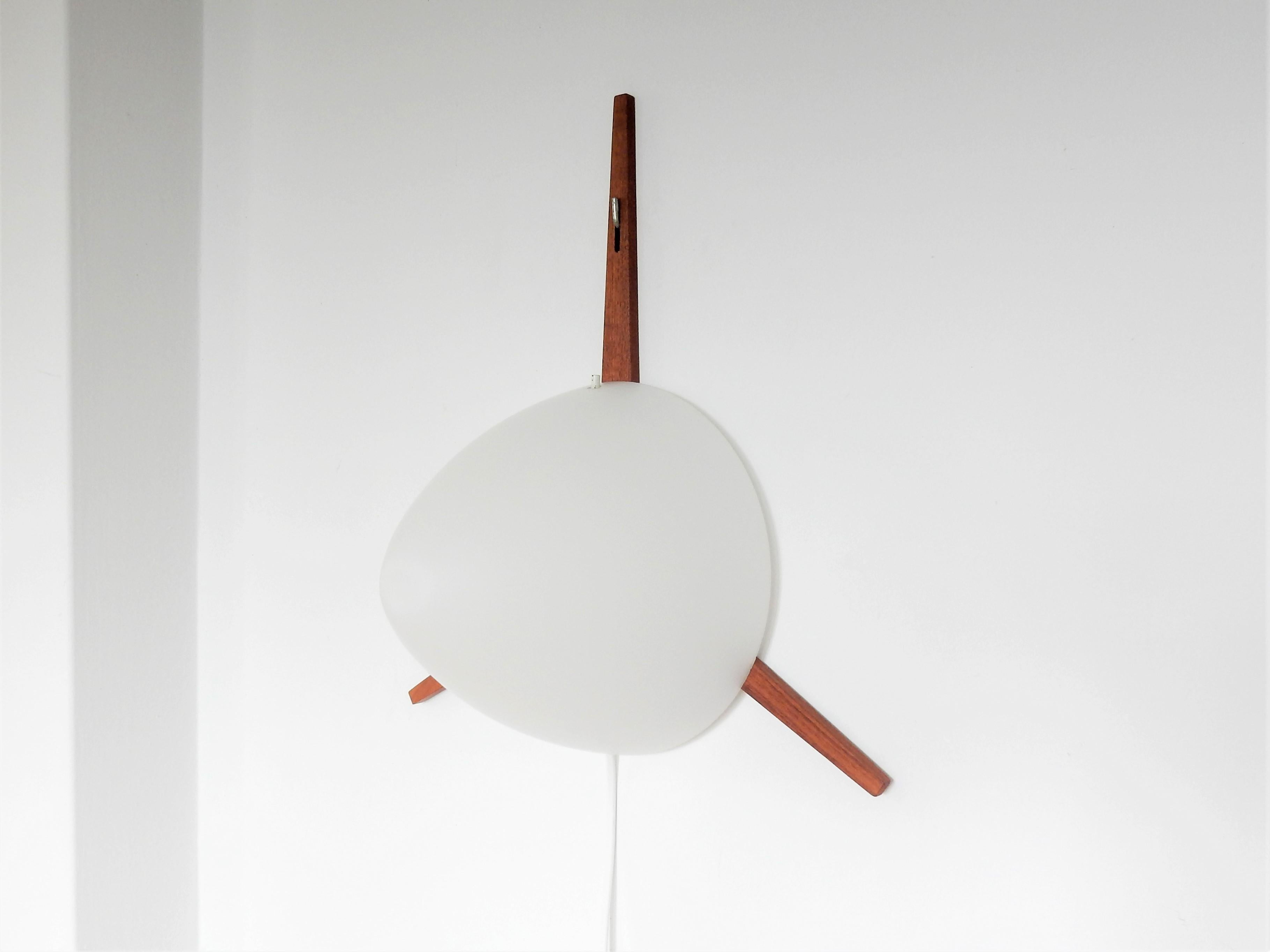 This elegant and very rare wall lamp was designed by Eje Ahlgren for RAAK in 1957. It is made of a teak wooden star shaped frame with a metal hook that holds the opaline glass cone shaped shade. Very simple though very warm and playful design. These