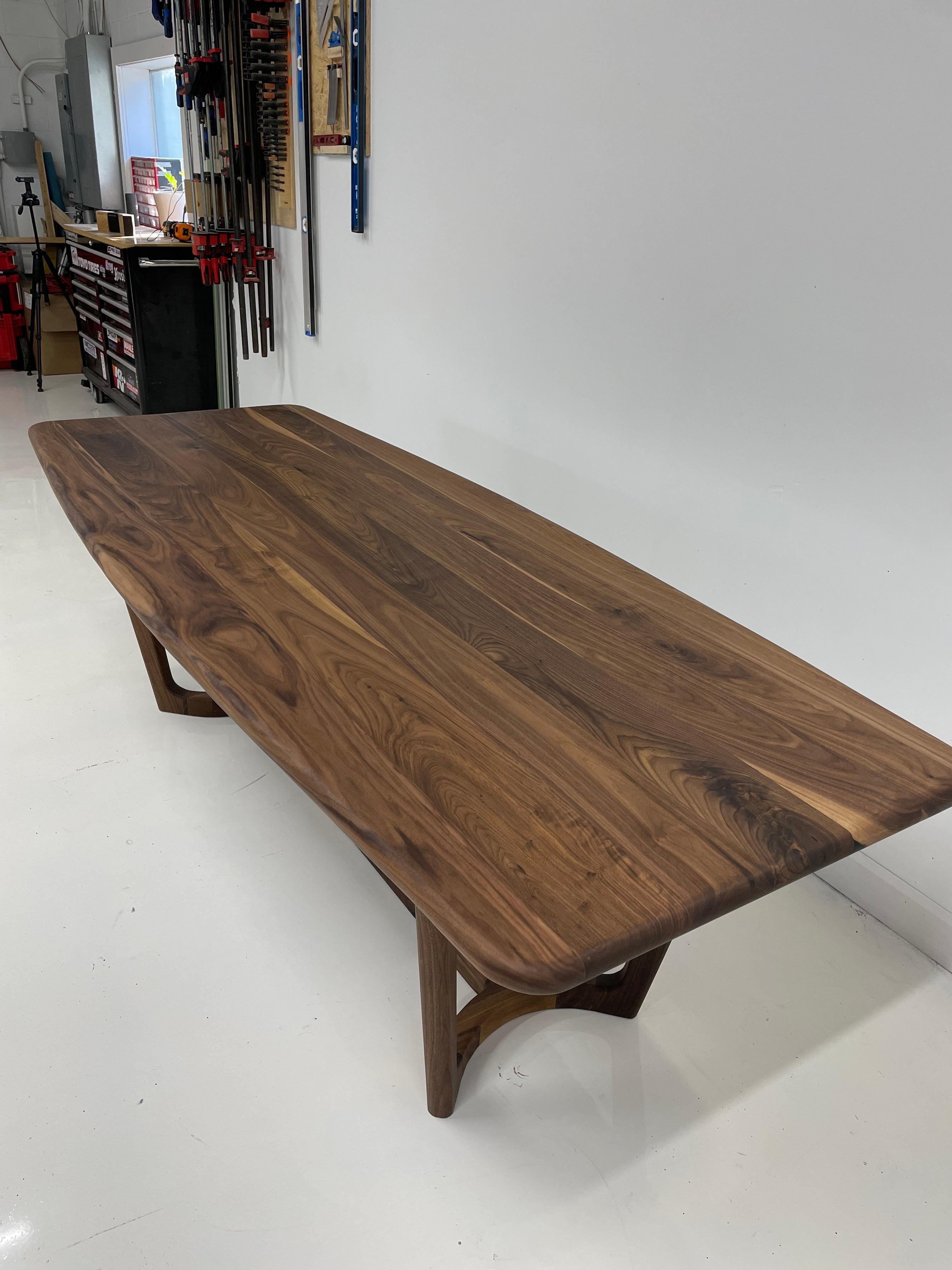 A beautiful Mid-Century Modern take on the dining table. Made out of solid Walnut, this table is made without a single sharpe edge giving it soft feel and keeping your space feeling light. A slight curve to the table top and gently tapered legs all