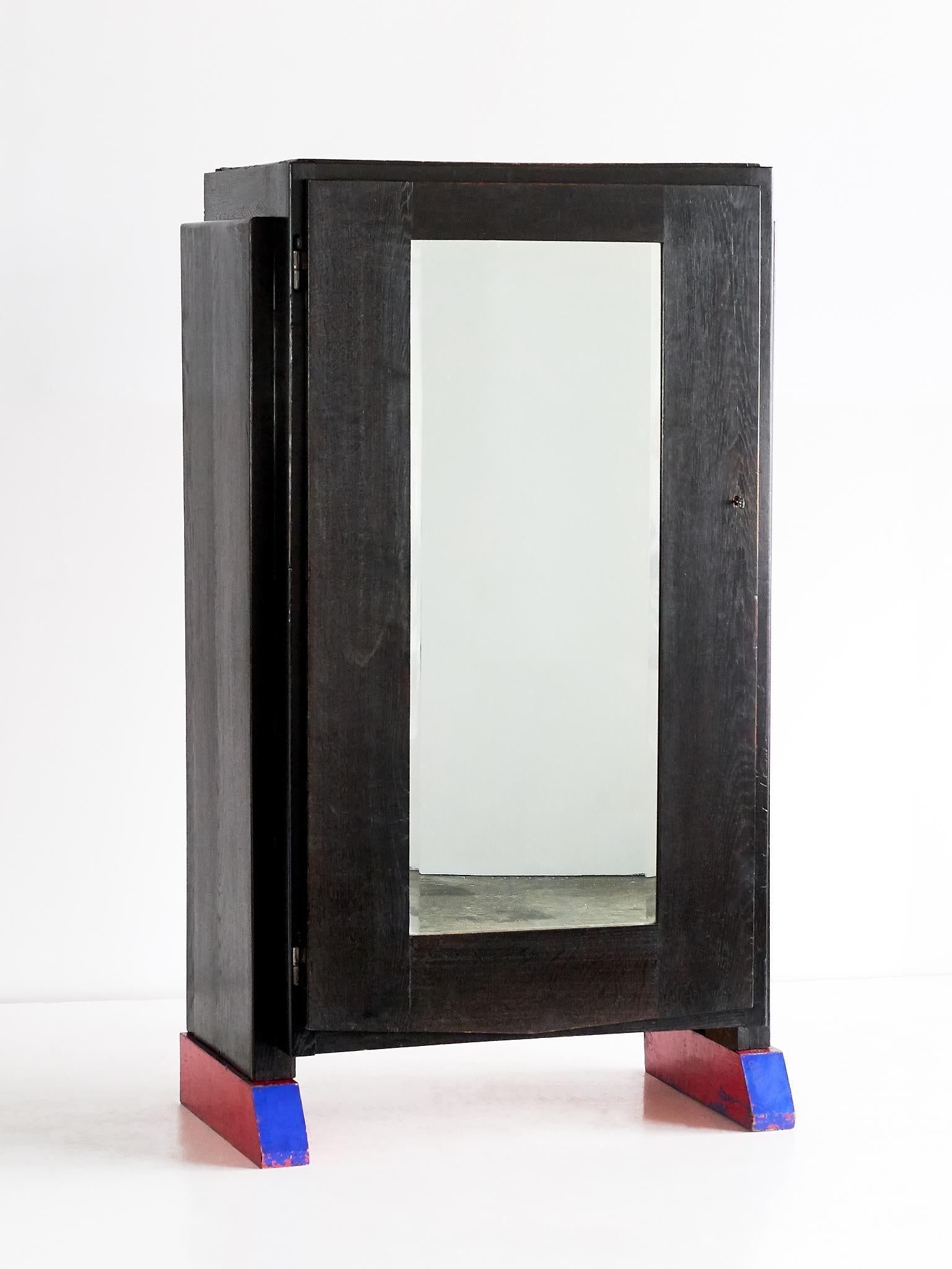 This unique wardrobe cabinet was designed and executed by Hildo Krop for his own home, circa 1930. The large cabinet is made of black stained oak with lacquered red and blue oak legs and a mirror door. The cabinet was made by Krop in his own