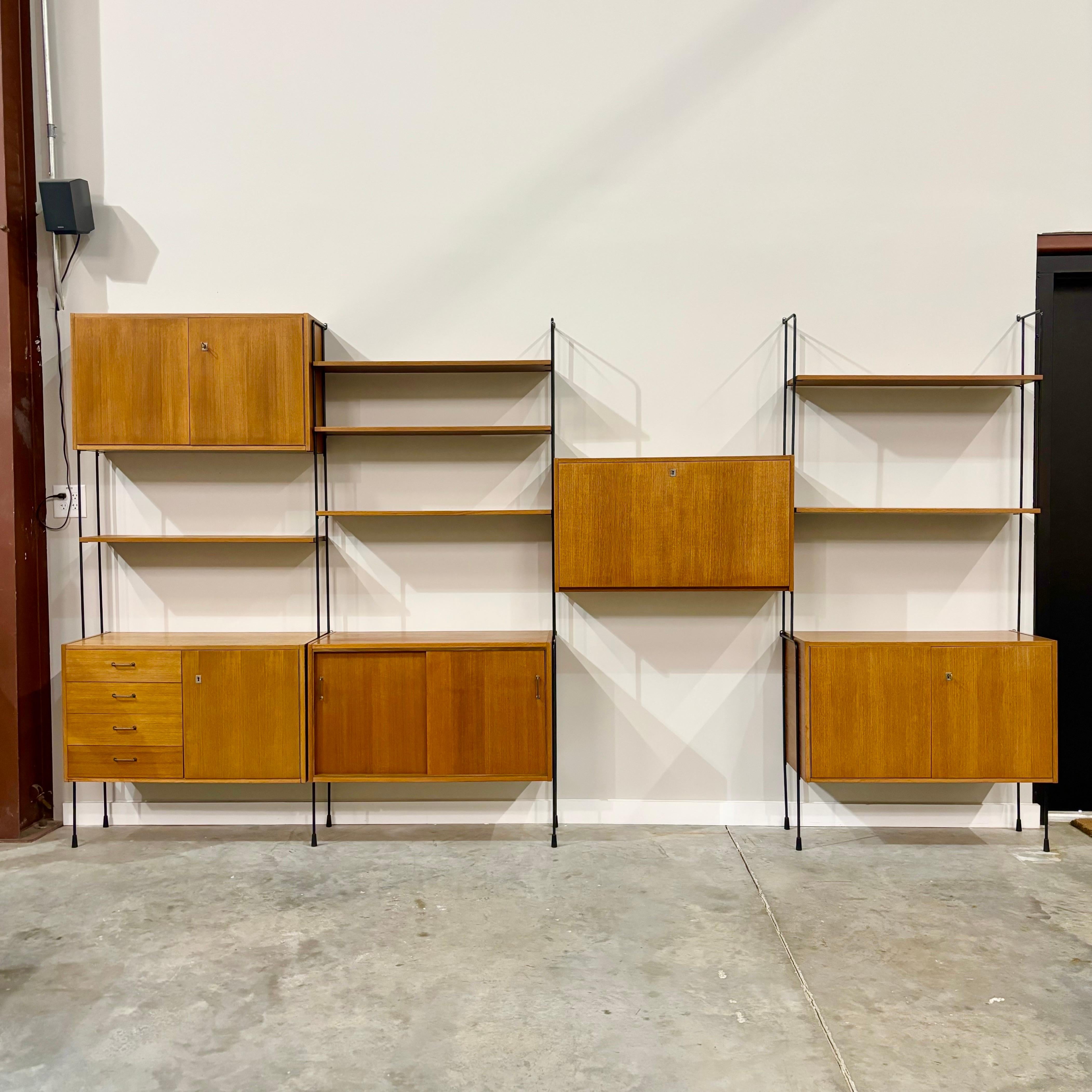 Vintage four-bay wall unit by Hilker of Germany, circa 1960.  Wall mount steel frame with teak cabinets and glass clad bar cabinet.