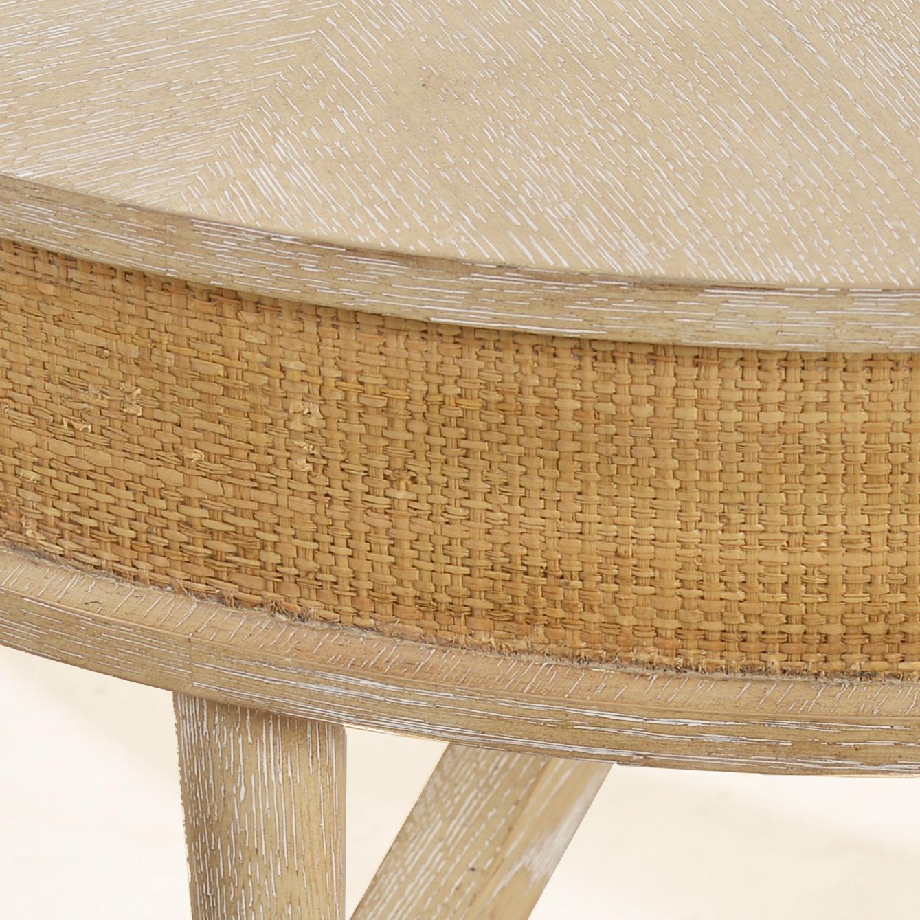 Cette élégante table de style Coastal présente la finition ElegS, un plateau rond en bois avec un tablier enveloppé de raphia, ajoutant chaleur et sophistication. Les pieds ronds et effilés sont reliés par un châssis façonné, tandis que les viroles