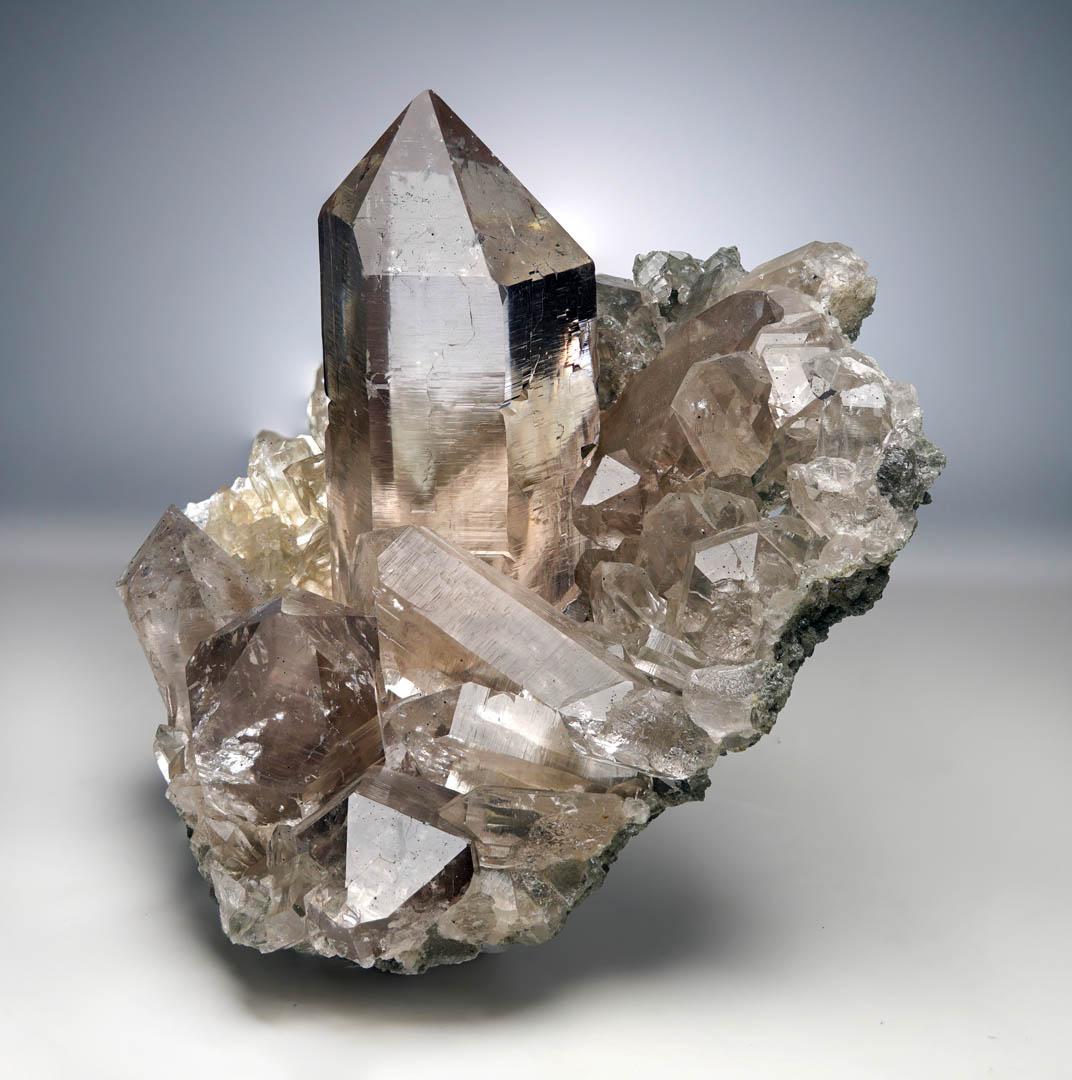 Di altissima qualità, proveniente dalle vette dell'Himalaya, questo gruppo di quarzo cloruro di qualità museale, unico nel suo genere, presenta una terminazione perfetta di 3,5 pollici di diametro che si protende verso il cielo, incorniciata da una