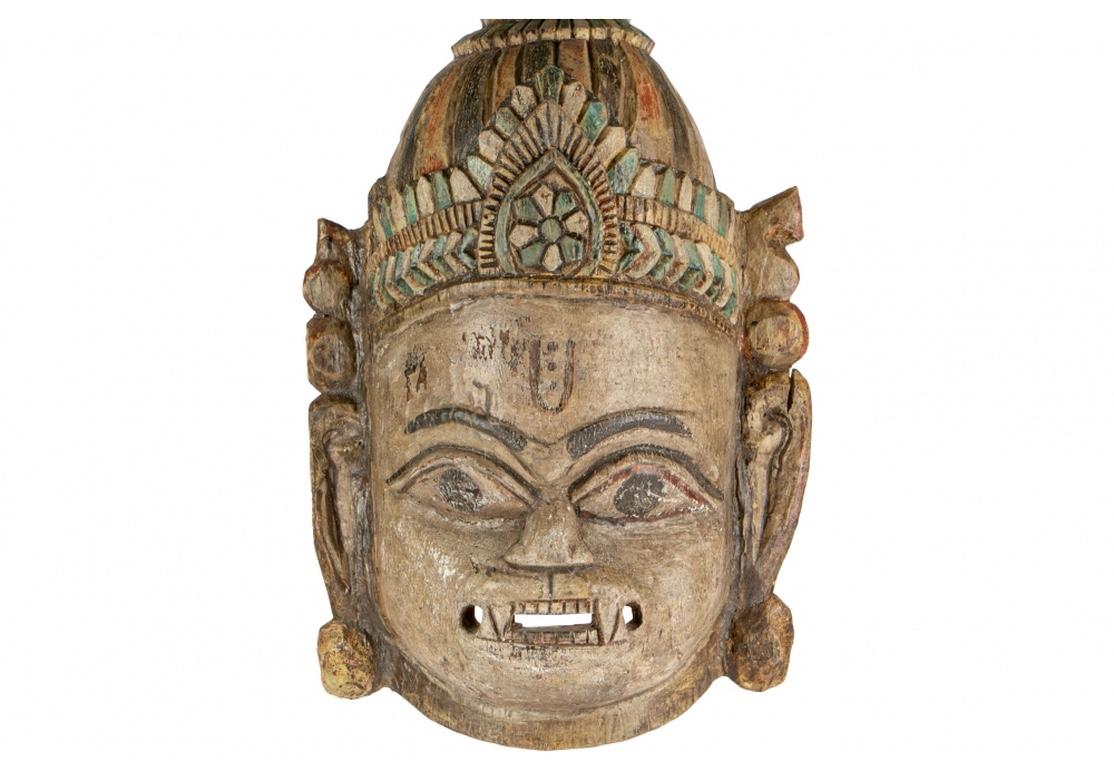 Hanuman, the monkey god and symbol of the always agitated human mind. A fierce face wearing a tall multicolored painted headdress, with long ears. Painted motifs on the forehead (worn). With a wire on the back for hanging.
On a fine metal mount