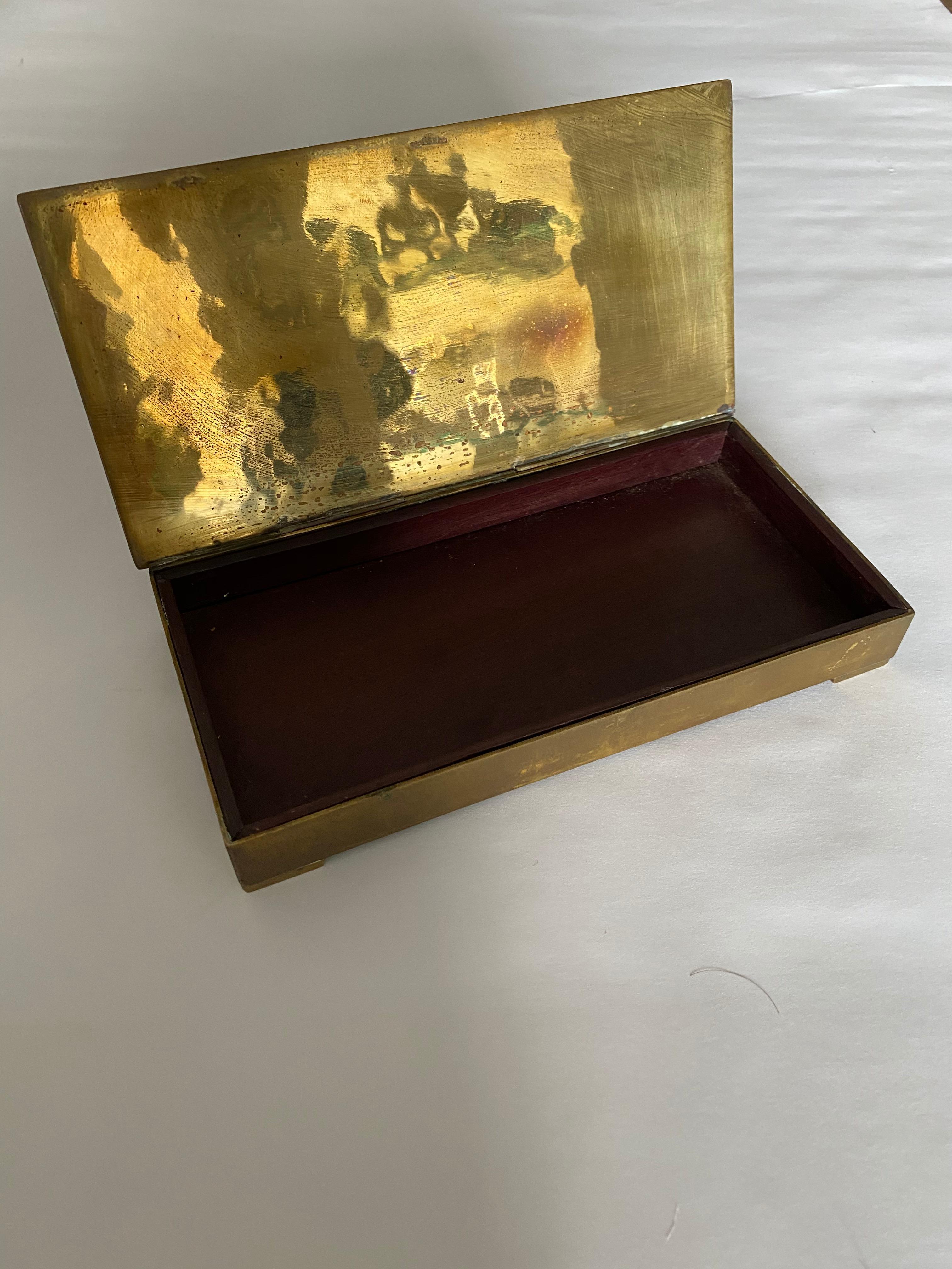 Caja metálica de latón con incrustaciones de malaquita y sodalita (o lapislázuli) con bisagras e interior de palisandro. Una pirámide azteca y montañas adornan la tapa. Los herreros metalúrgicos de Taxco Mexico eran conocidos por producir este tipo