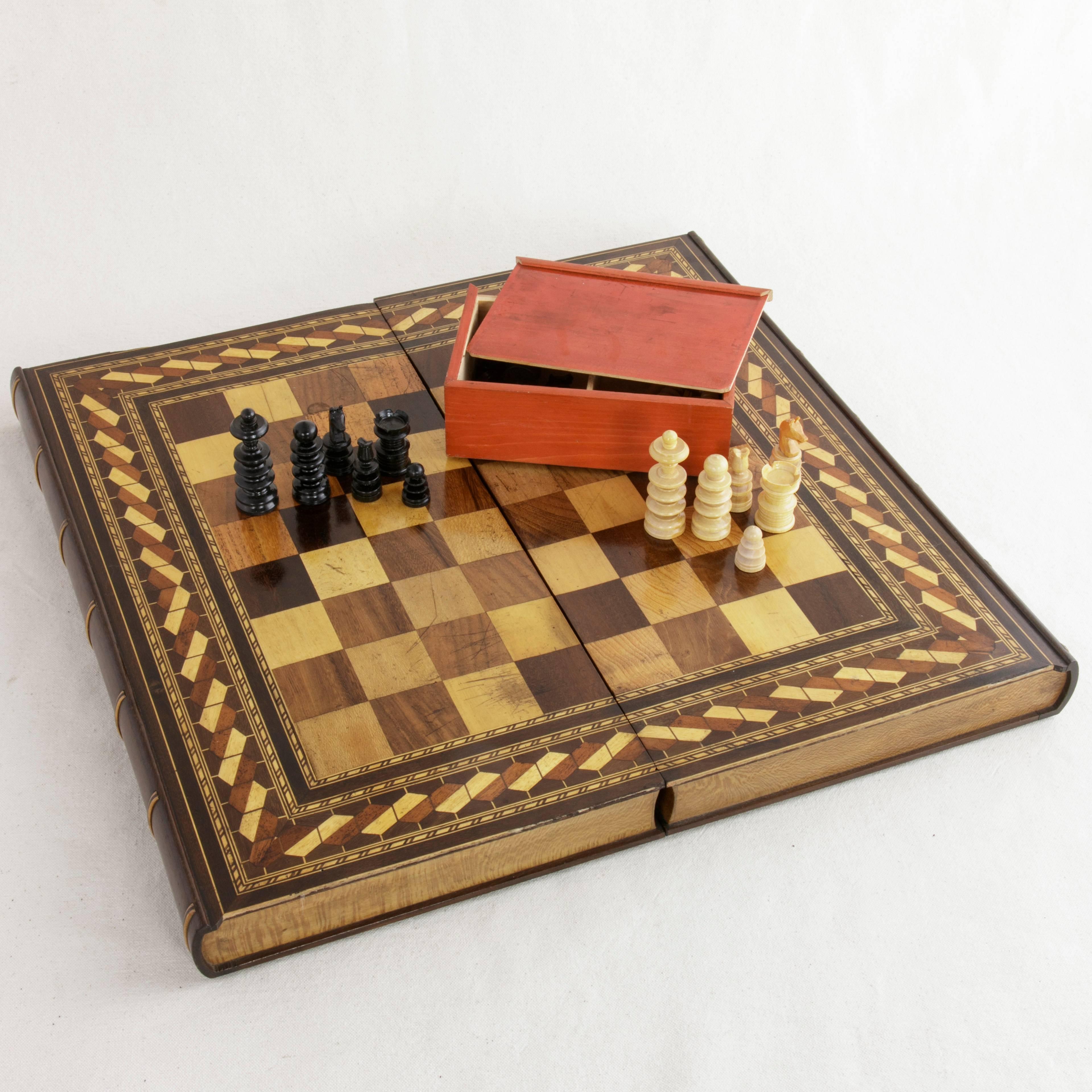 Taking the form of two stacked books, this hinged marquetry game box features a chess and checker board on the exterior and marquetry backgammon board on the interior. Displaying intricate inlay of exotic woods in geometric patterns, this box