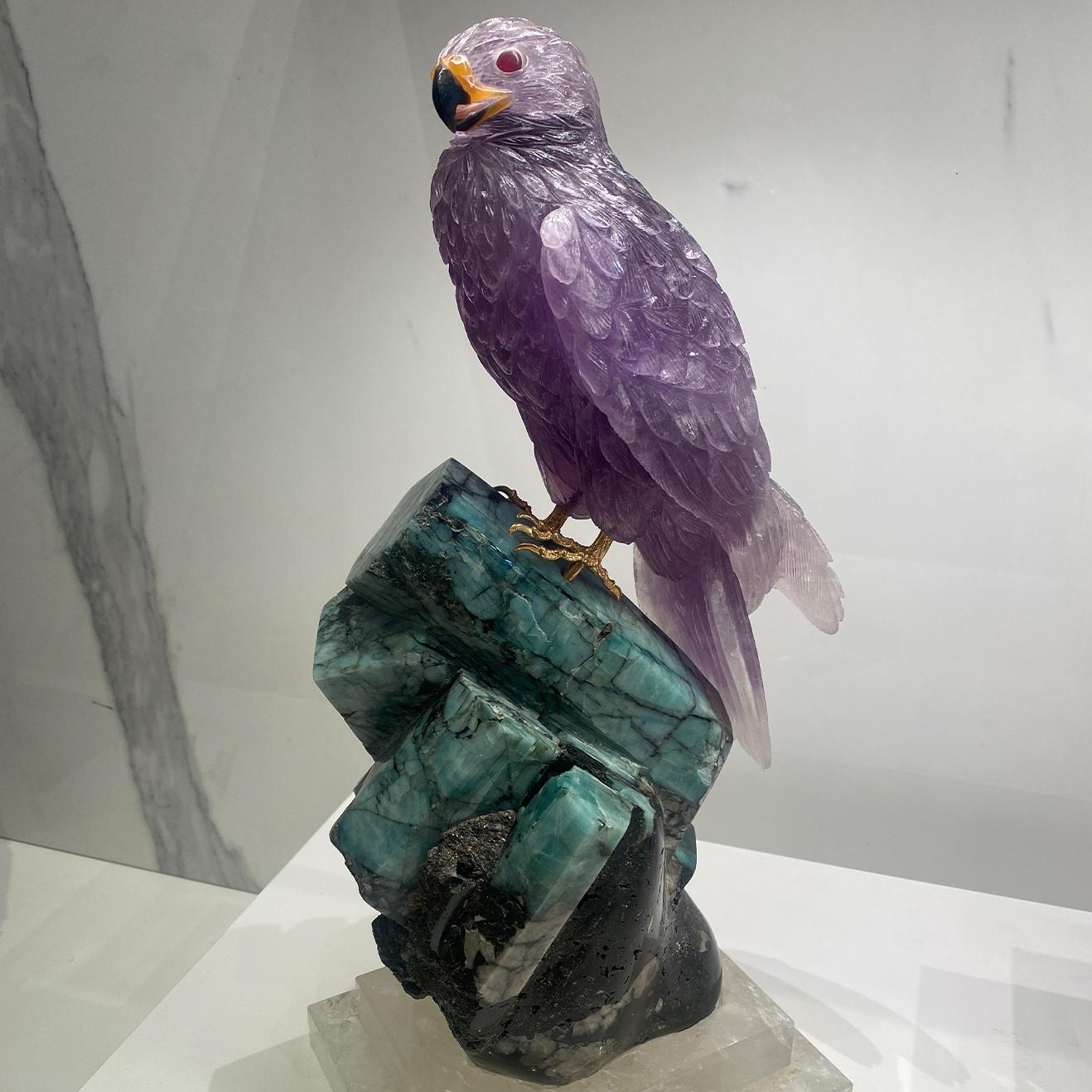 A rare, one-of-a-kind sculpture of a hand carved amethyst falcon, perched atop an emerald crystal base, stabilised by a platform carved from fine natural quartz crystal.

- A hand carved falcon using fine quality natural amethyst crystal
- The