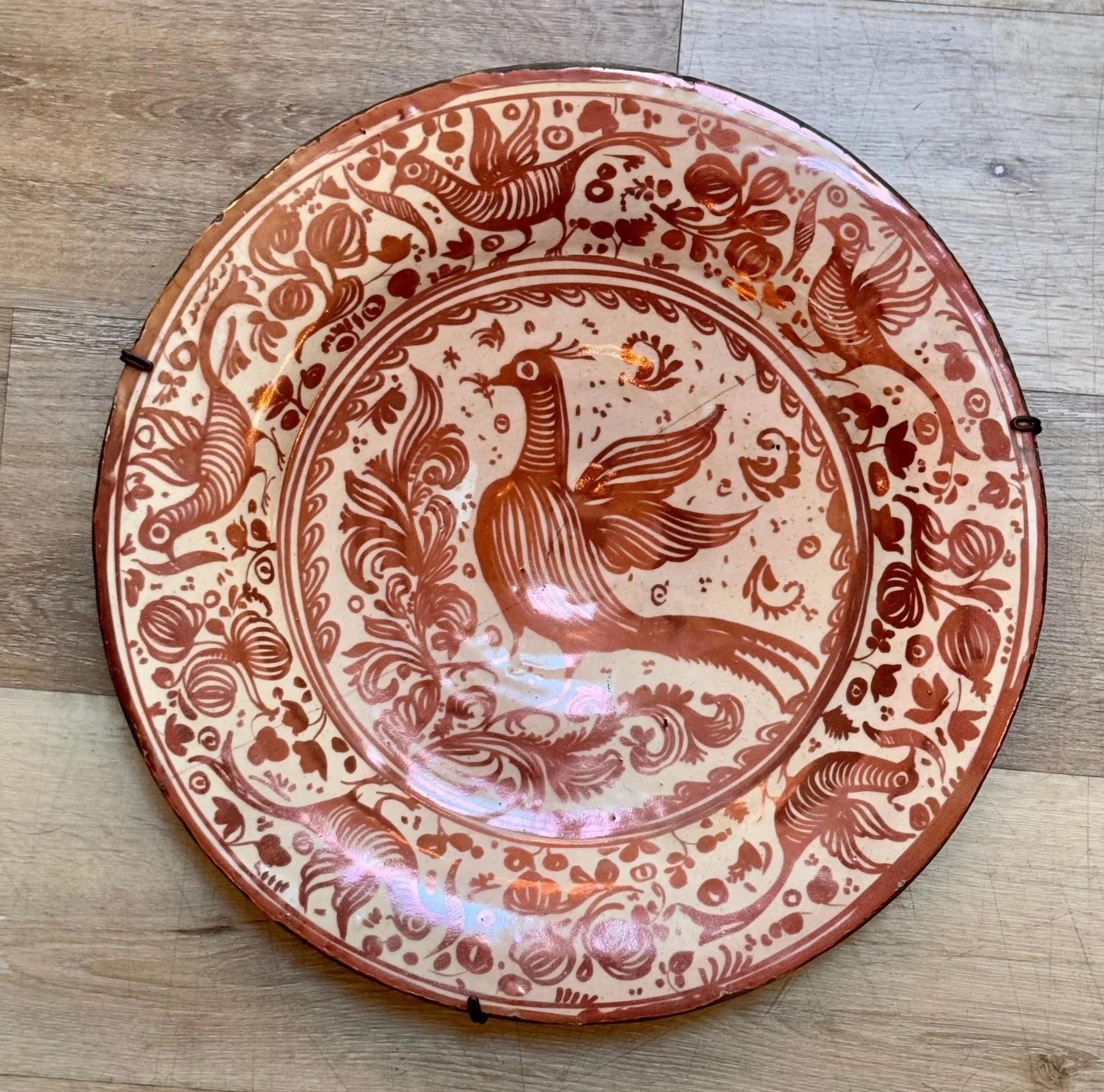 Particulièrement grand chargeur en cuivre lustré hispanique moresque du 17e siècle, avec  un bord en bandeau décoré d'oiseaux et d'un motif floral en forme de grenade. Le centre est peint d'un oiseau stylisé à longue queue tenant une brindille sur
