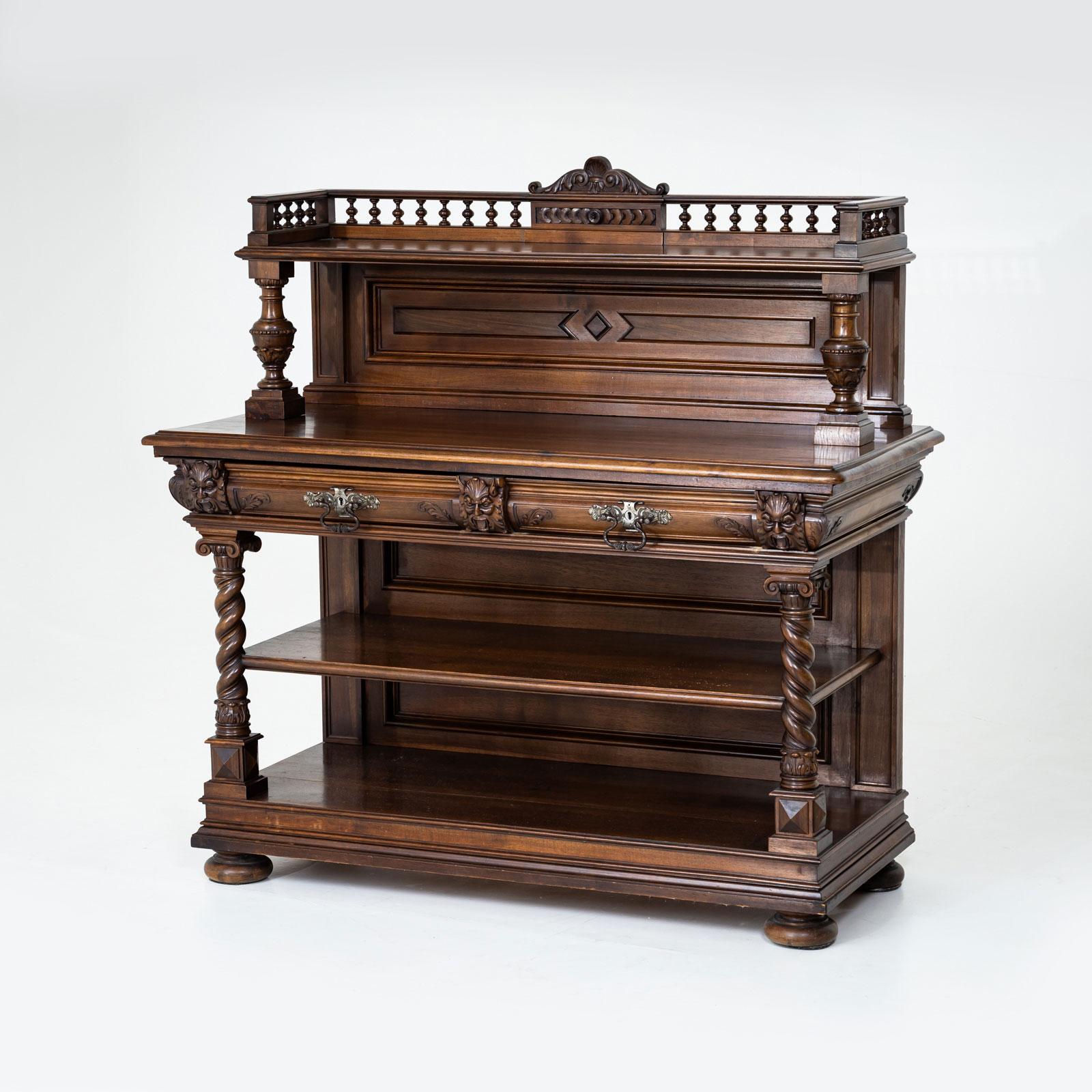 Un sorprendente buffet storicista in noce, realizzato in Germania alla fine del XIX secolo. La credenza è caratterizzata da colonne tornite, colonne a balaustro intricatamente intagliate e maschere a vento decorative, con una piccola ringhiera che
