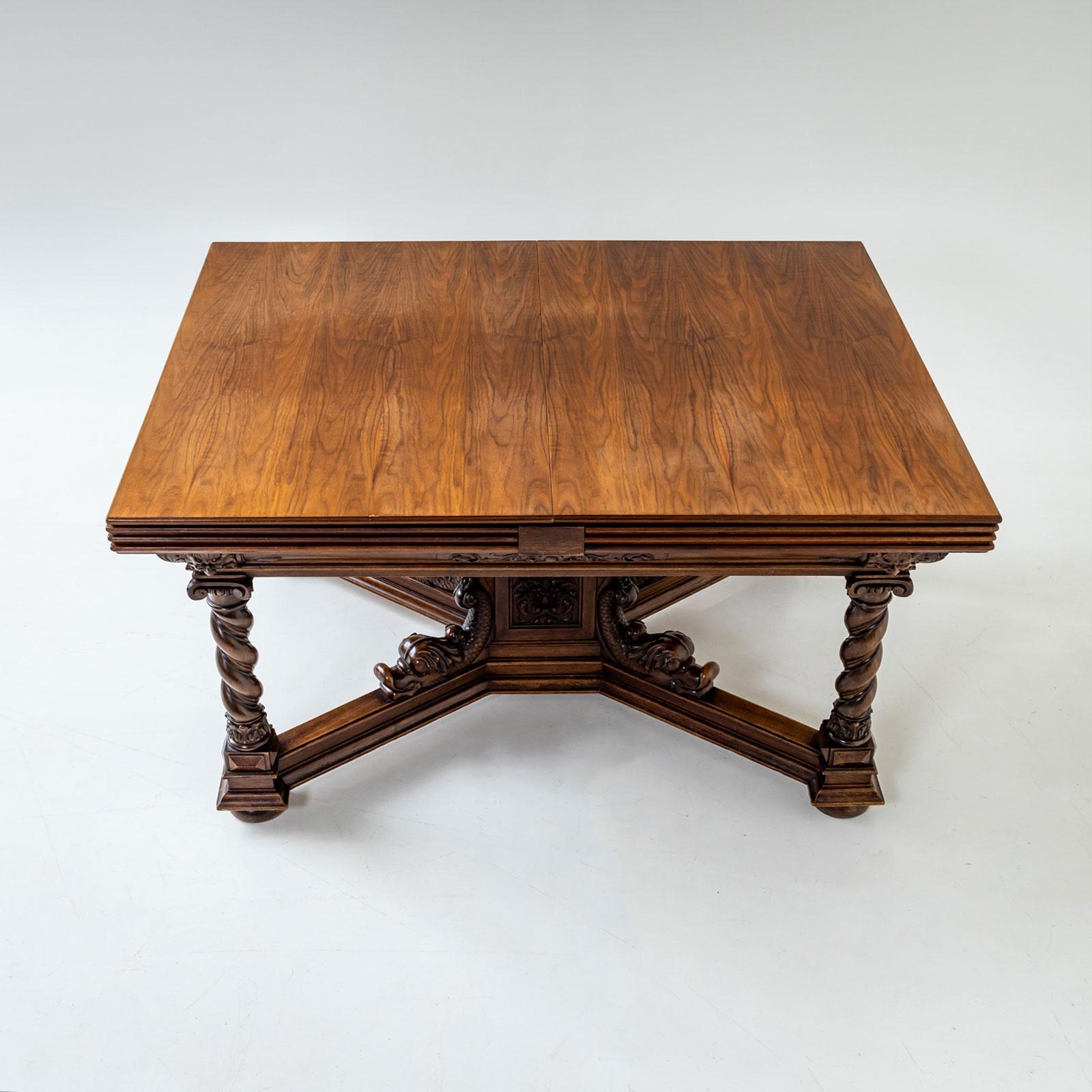 A large extendable table from the Historicist period, crafted in walnut, with an impressive length of up to 572 cm when fully extended. The table features intricately turned column legs and a central octagonal pedestal adorned with carved dolphins