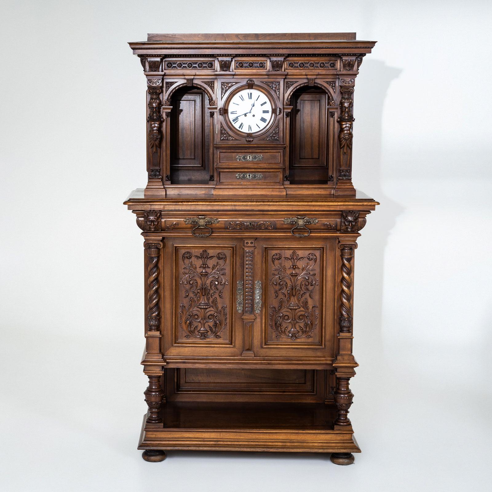 Una grande credenza storicista con orologio, realizzata in Germania alla fine del XIX secolo. La parte inferiore presenta due ante e un ampio cassetto, riccamente ornato da decorazioni intagliate, semicolonne tornite e gambe a balaustro decorative.