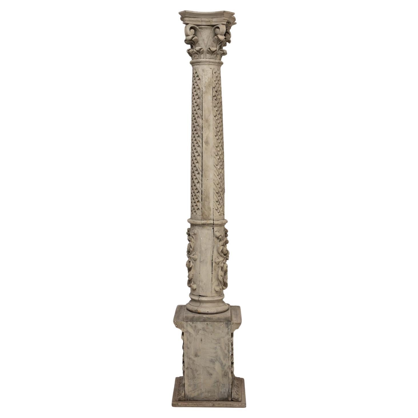 A tall historicist column crafted from carved wood, dating to the 19th century. The column is painted in gray and rests on a square base. The shaft is richly adorned with scale-like patterns and winged cherub heads, adding a decorative and symbolic