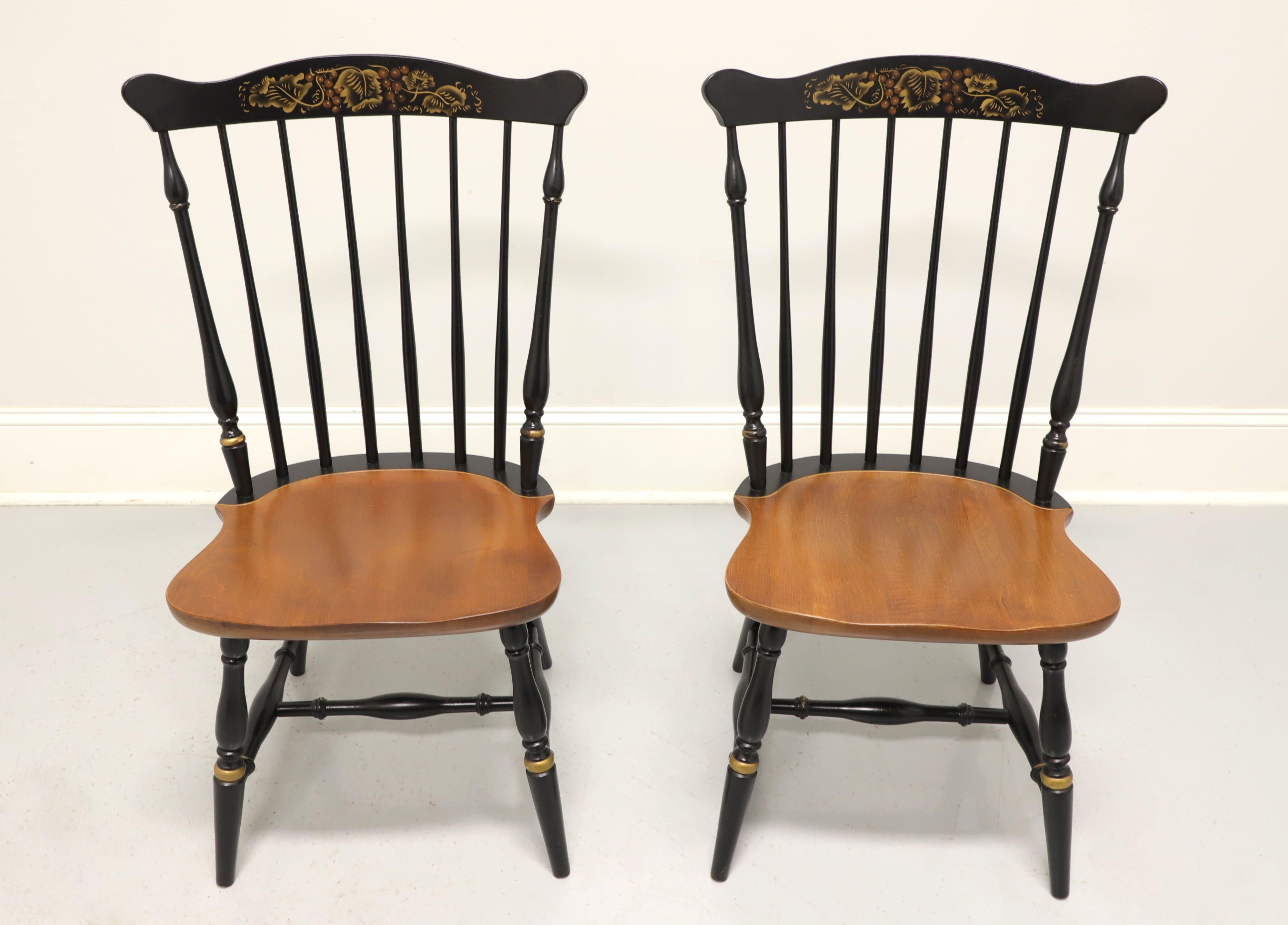 A pair of Windsor style dining side chairs by Hitchcock Chair Co. Solid maple with black lacquer, decorative stenciling to crest rail, gold accents, spindle backs, maple seat, turned legs and stretcher base. Made in Connecticut, USA, in the mid 20th
