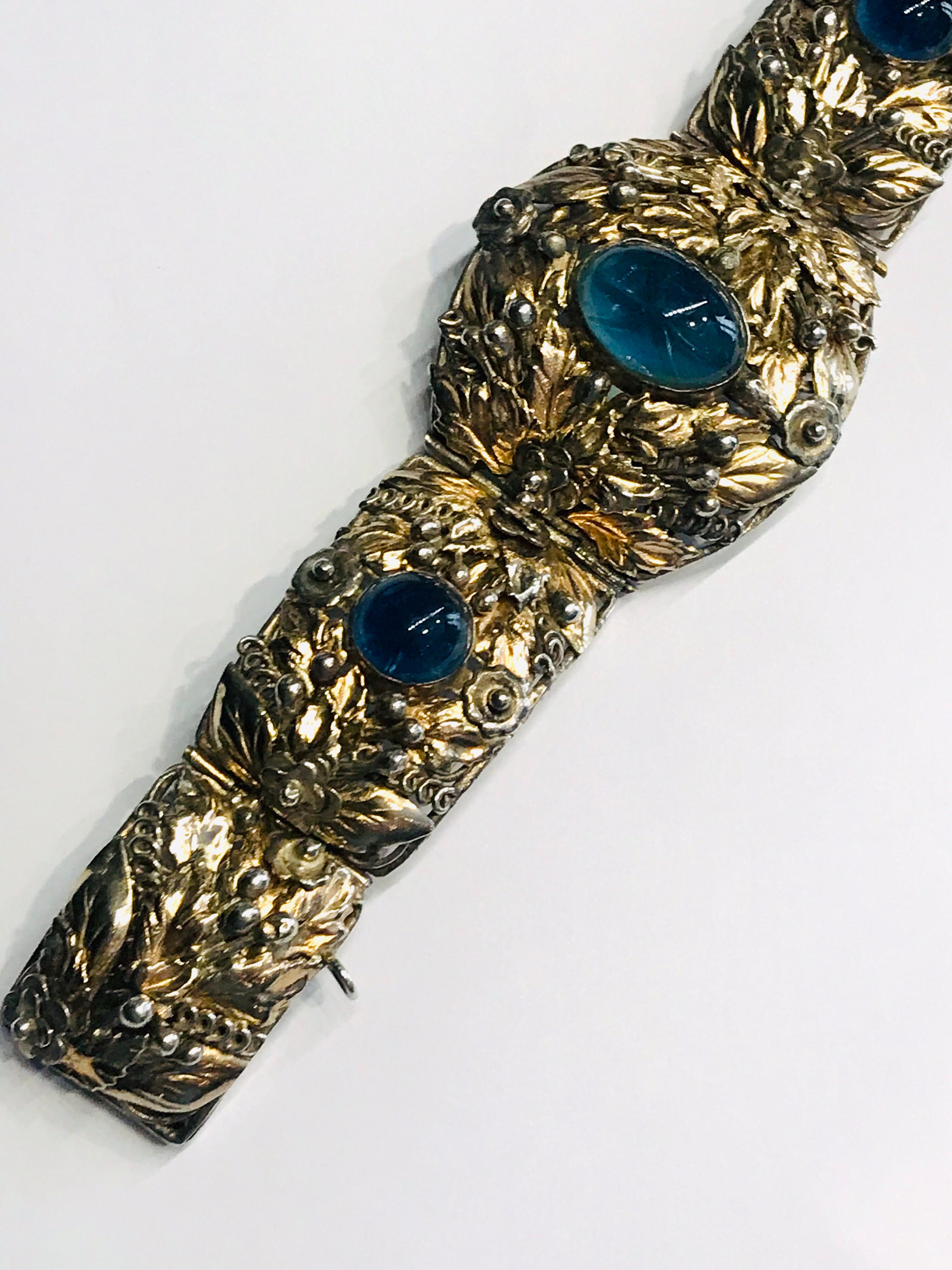 A beautifully constructed hand made bracelet by famous American jewelry company Hobe' between 1941 and 1947. The bracelet has an intricate foliate design of gilt leaves, berries and curled vines on six panel links. Mounted with three blue glass