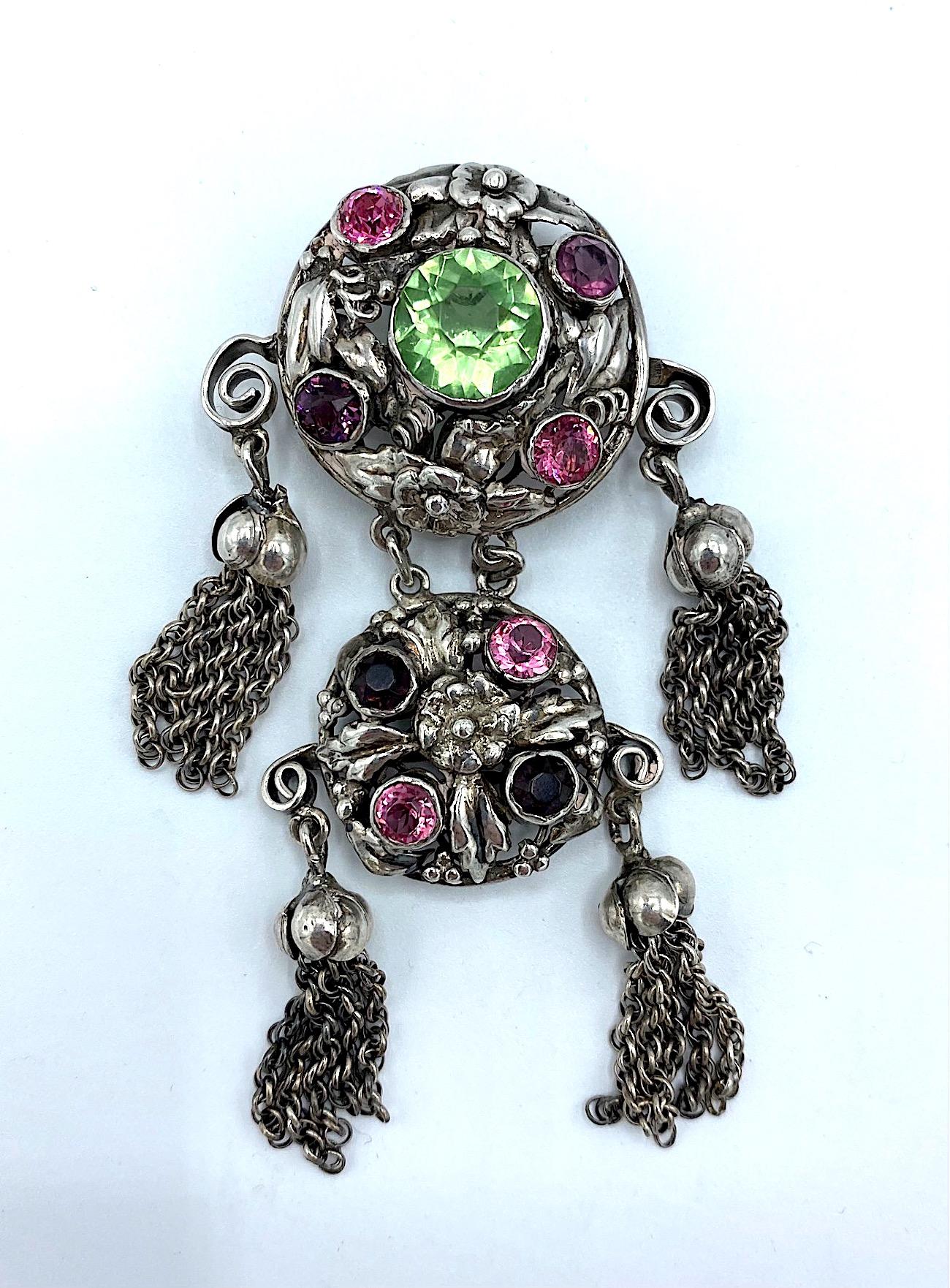 A stunning and intricate brooch by jewelry company Hobe' made between 1941 and 1948. It features two round disks of intricately hand made leaves and flowers within a round framework. The disks are set with pink, purple and green faceted crystal