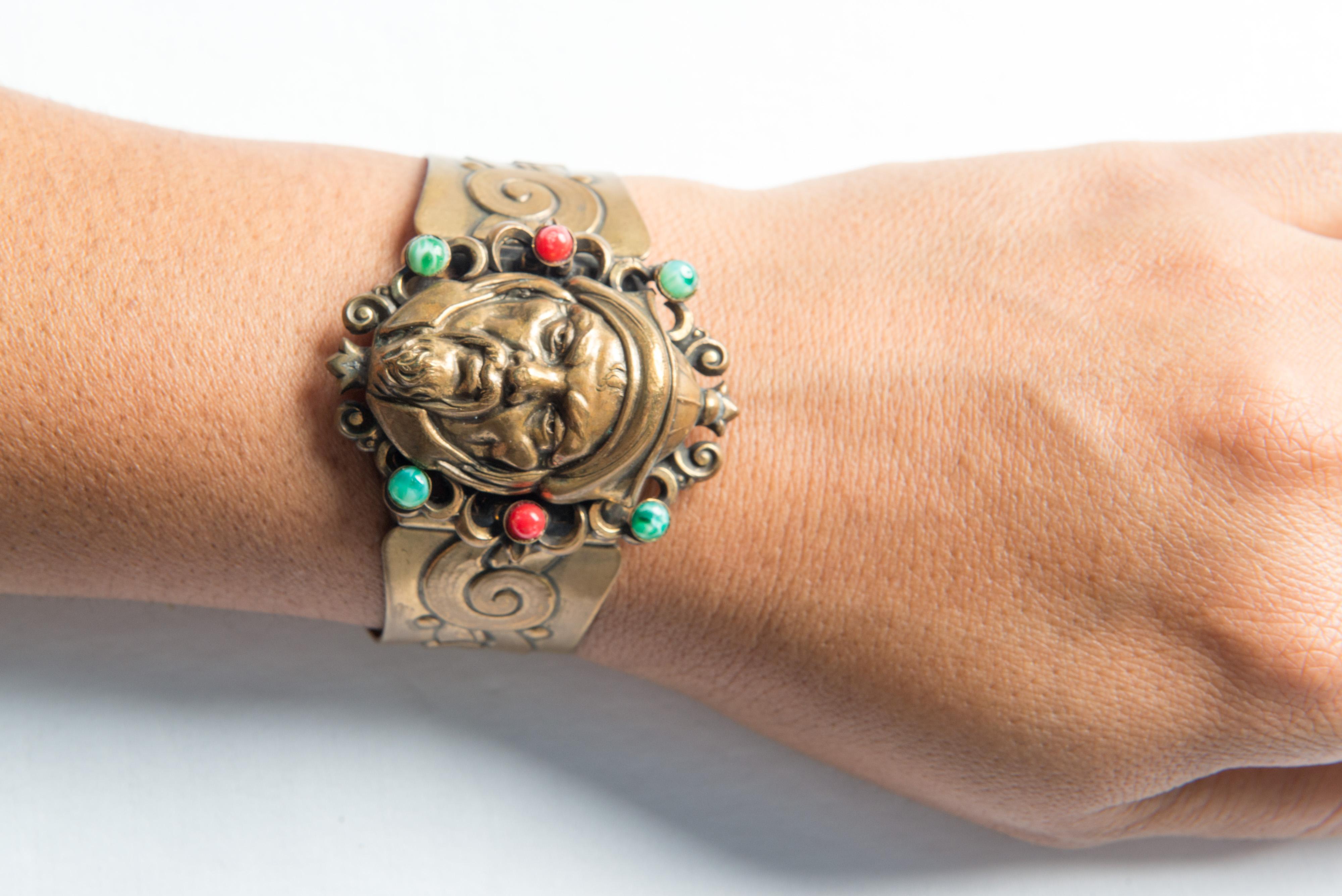 Expandable brass Hobe cuff with detailed face of a warrior decorated with three red jewels and three blue jewels. Safety chain is missing. Signed. 