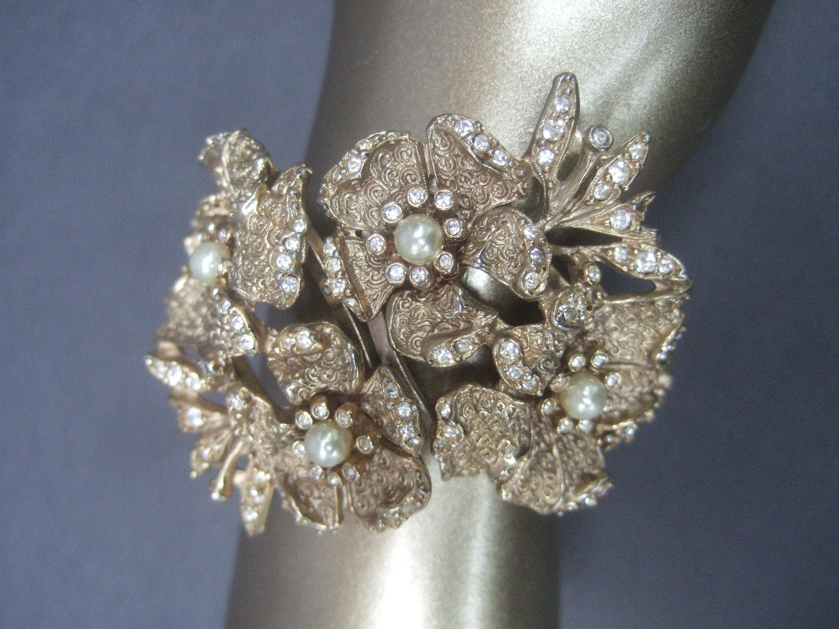 Hobe' wide gilt metal jewel encrusted hinged cuff bracelet c 1960s
The large scale floral bracelet is embellished with clusters of resin enamel faux pearls; juxtaposed with tiny diamante crystals scattered across the collection of flower pedals

The
