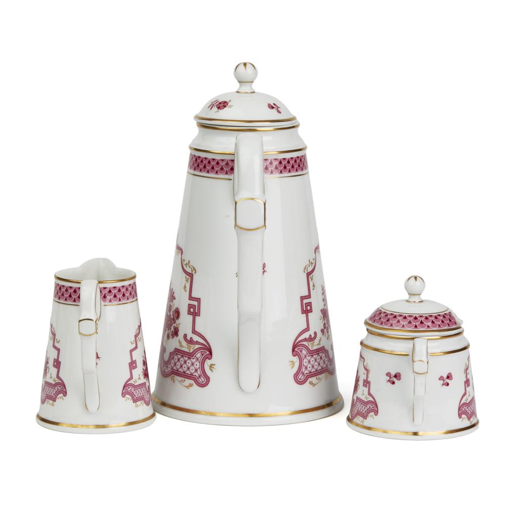 A fine German porcelain Höchst three part coffee set in the Classic pattern, the stylish set decorated in puce with gilding highlights and comprising of a tall cylindrical shaped lidded coffee pot, similar shaped cream jug and a twin handled lidded