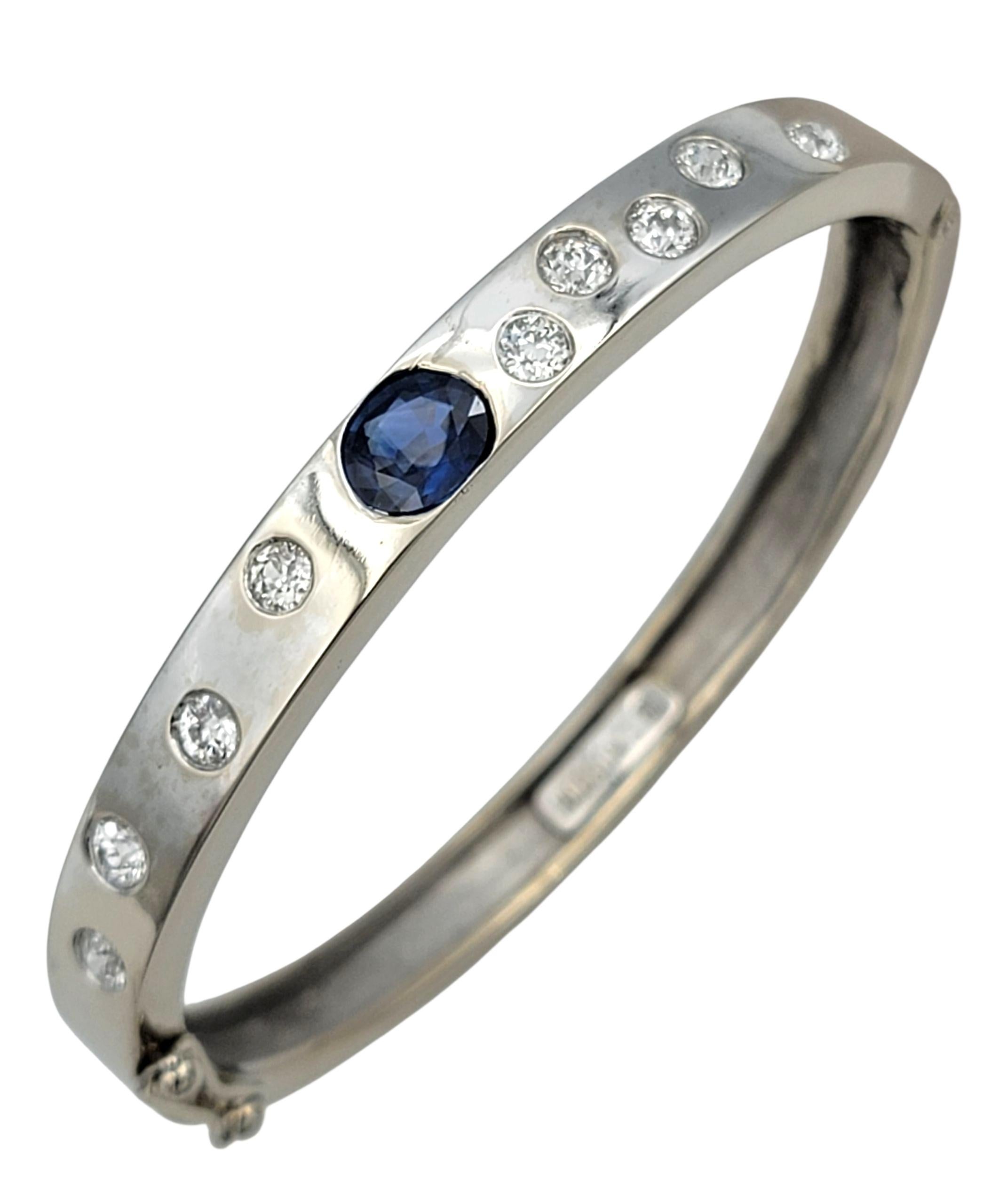 Questo splendido bracciale bangle con cerniera di Hodson's è realizzato in oro bianco 14 carati e sfoggia un design audace incentrato su un ricco zaffiro blu naturale dal taglio ovale. La tonalità audace dello zaffiro e la sua forte saturazione