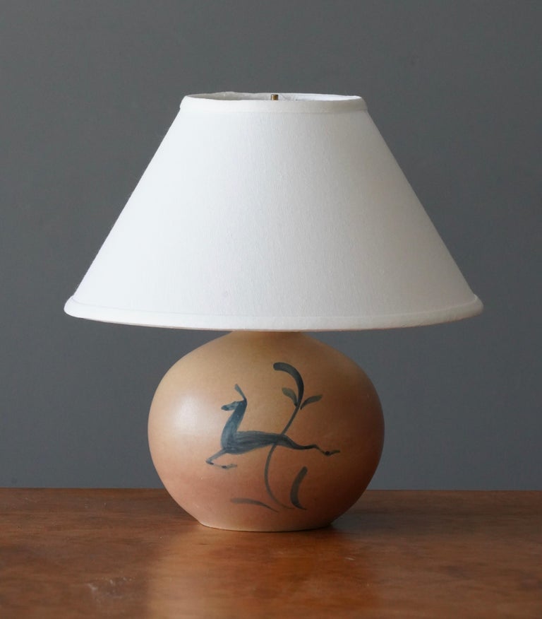 A table lamp by Höganäs, features pink / beige glazed earthenware. Handpainted details in blue. 

Dimensions listed are without lampshade. Sold without lampshades.
Dimensions with shade: height is 12.5 inches, width is 12.25 inches.
Dimensions