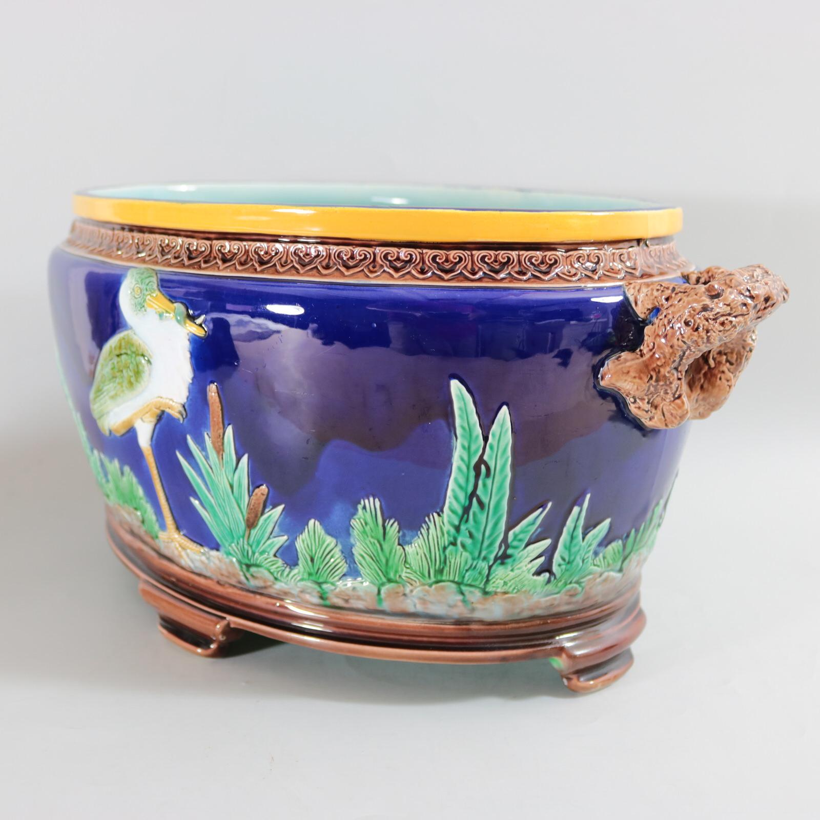 Holdcroft Majolica jardinière which features a heron stood holding prey, amongst bullrushes/cattails and foliage. Colouration: cobalt blue, green, brown, are predominant.