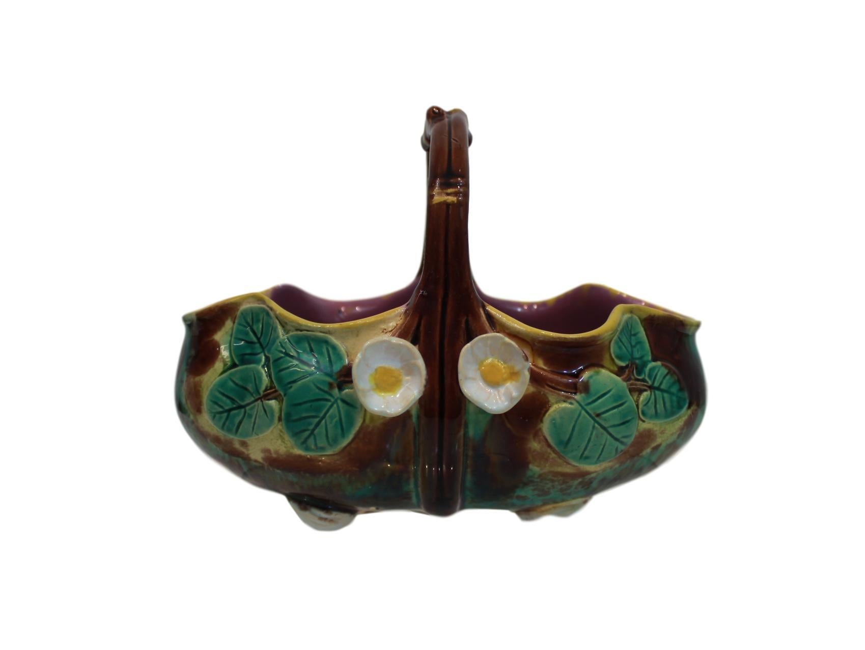Holdcroft Majolica pond lily basket, English, circa 1875, on a mottled green, brown and yellow ground, with green glazed leaves and two applied blossoms to each side, with twig-form handle, the interior glazed in pink.
Measurements: H 5.5 x W 4.5,