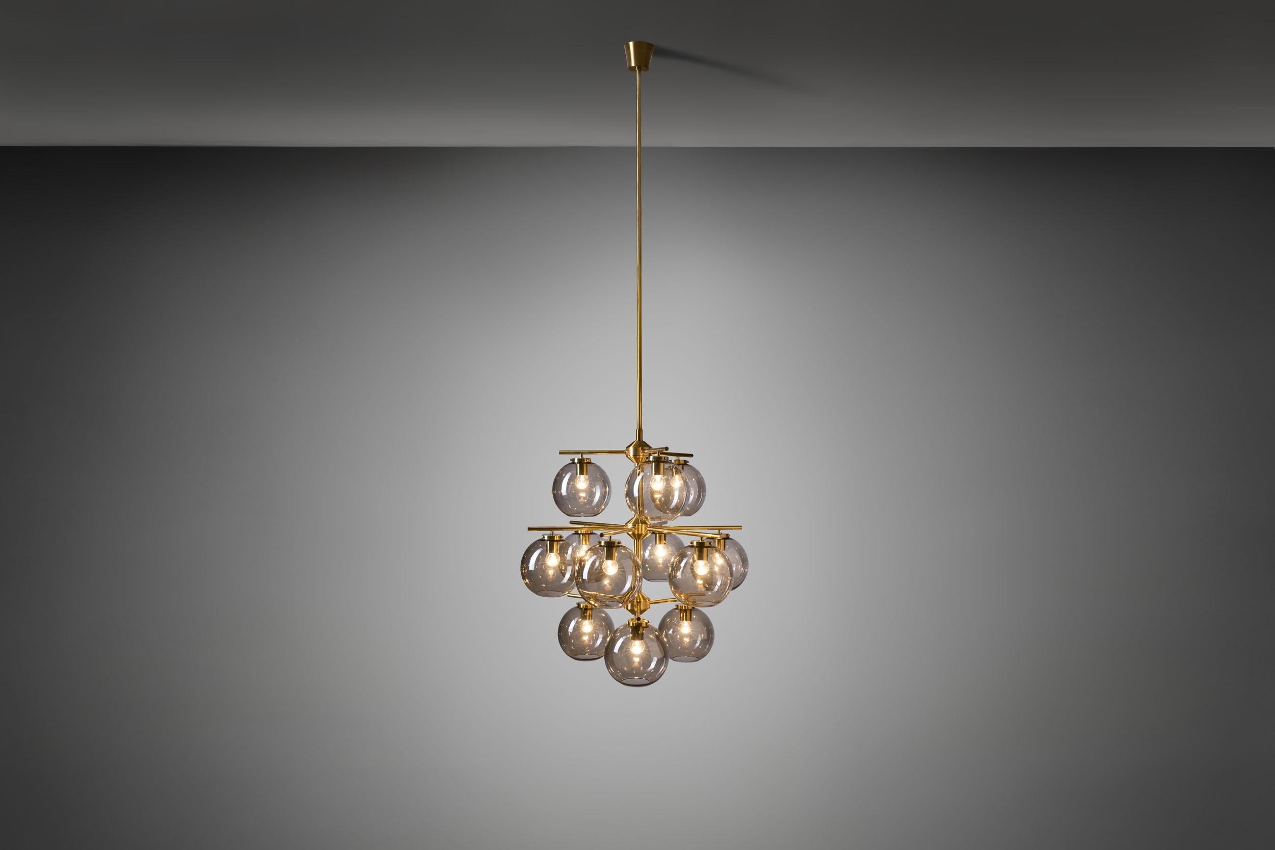 This marvellous chandelier is one of the most recognizable Swedish lighting designs of the mid-century era. With a brass frame holding 12 smoked, translucent glass shades, grandiose is the word to describe this model by. This model was designed by