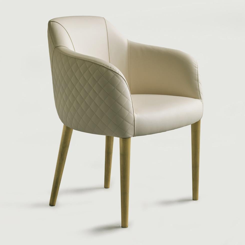 For ultimate sophistication and comfort in a modern dining interior, this gorgeous Deco-inspired Holly chair showcases a curved backrest and extended arm structure padded and upholstered in refined white leather. Embellished by an exquisite quilted