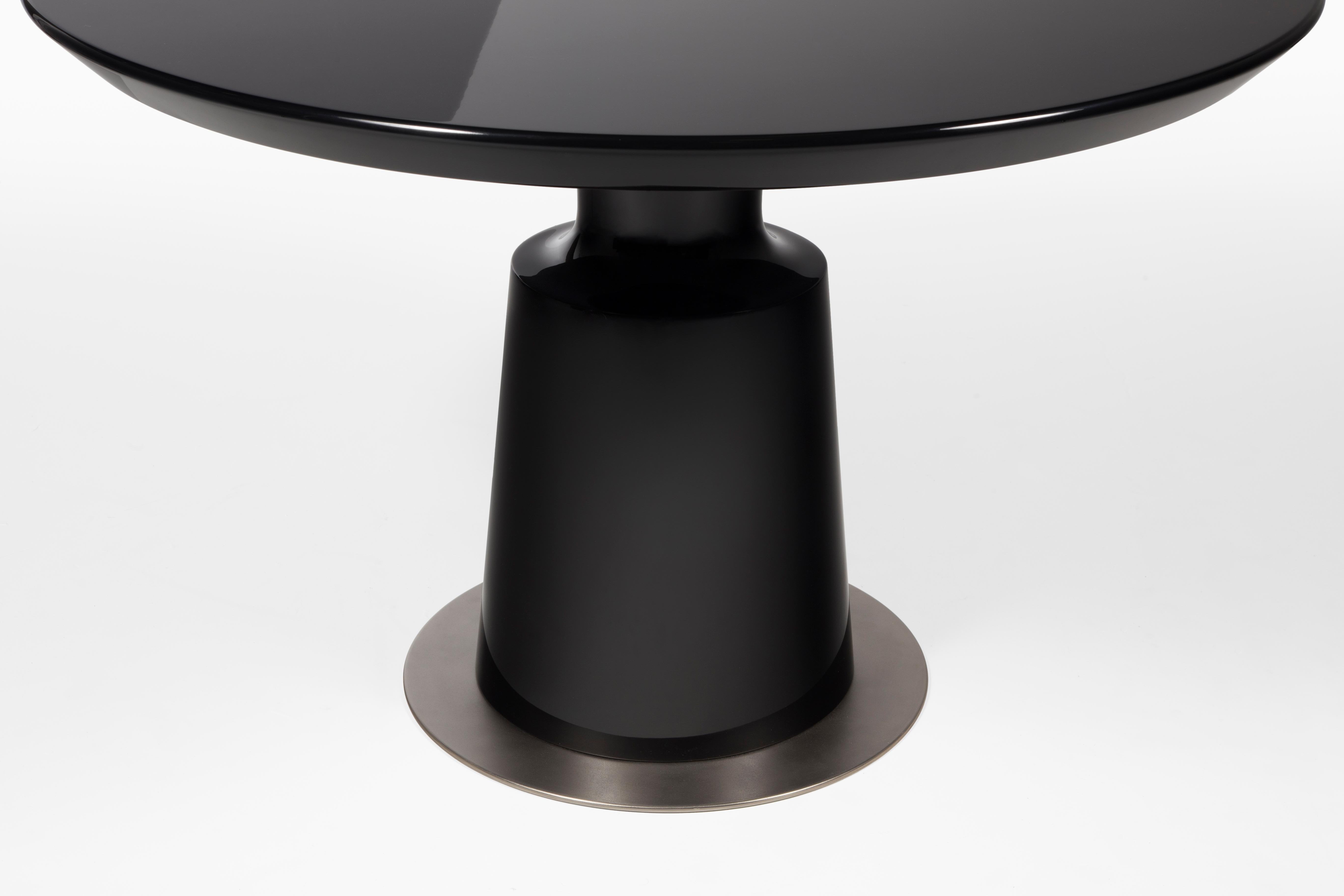 HOLLY HUNT Peso round dining table in black lacquer with aged nickel base plate. The curved shape of the Peso Dining & Side Tables is reminiscent of weights put on one side of a scale at pharmacies at the turn of the century. This table looks and