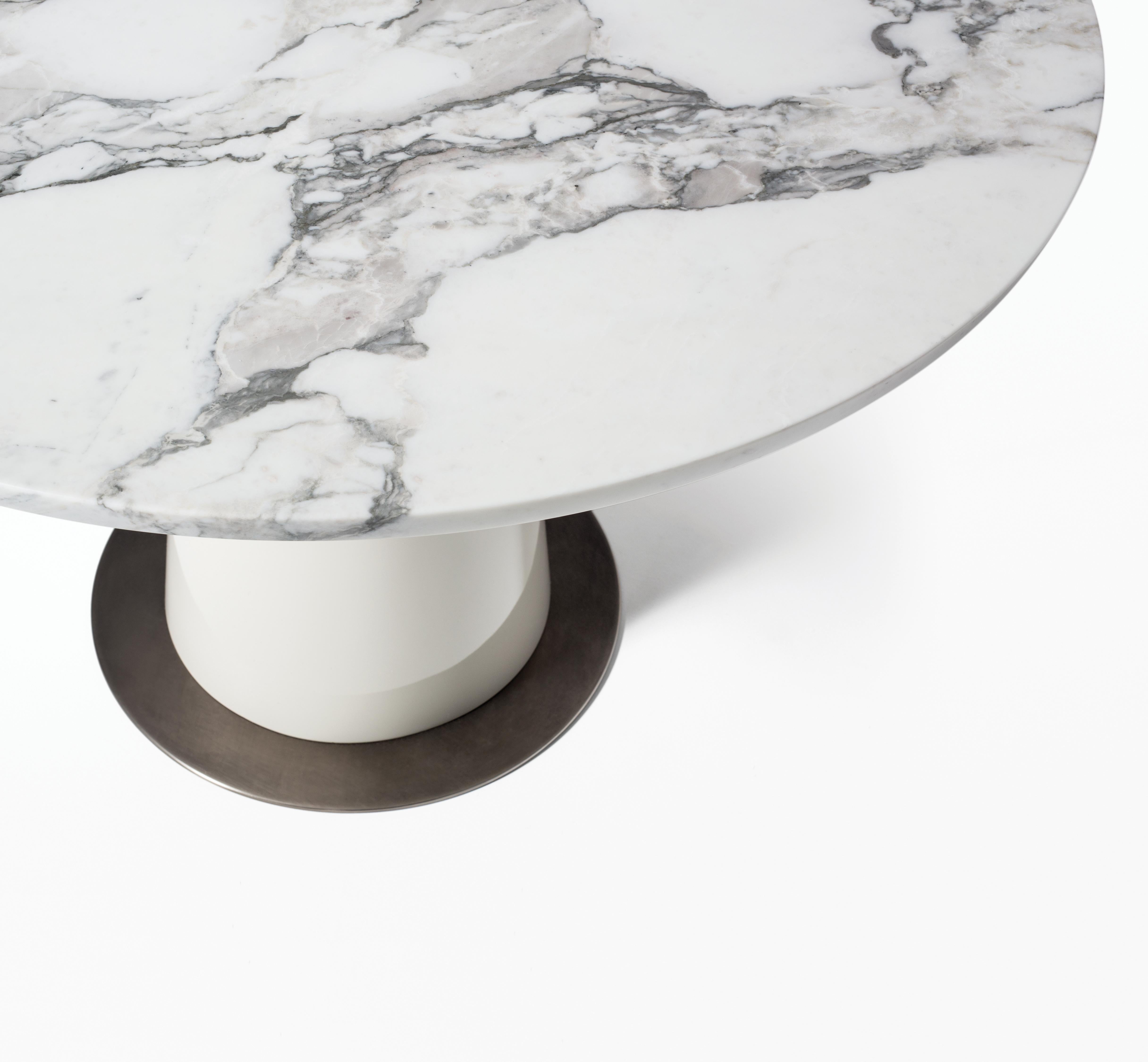 HOLLY HUNT Peso round dining table in stone with aged nickel base plate. The curved shape of the Peso Dining & Side Tables is reminiscent of weights put on one side of a scale at pharmacies at the turn of the century. This table looks and feels