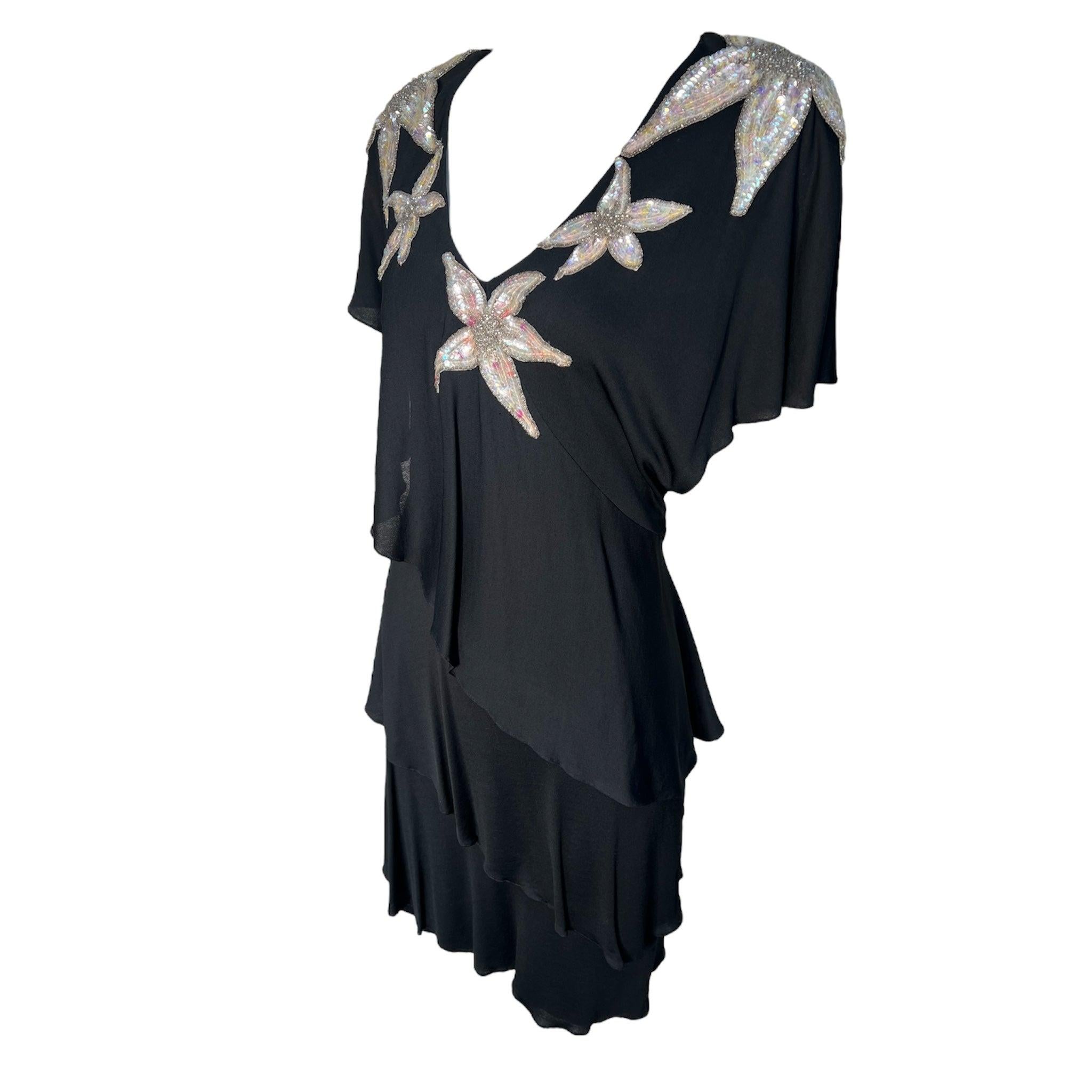 Le glamour de la fin des années 70 de la fabuleuse Holly Harp. Jersey de rayonne mat coupé en diagonales comme des pétales de fleurs. Des paillettes irisées et des perles argentées ornent le corsage et les épaules de fleurs aux pétales étoilés.