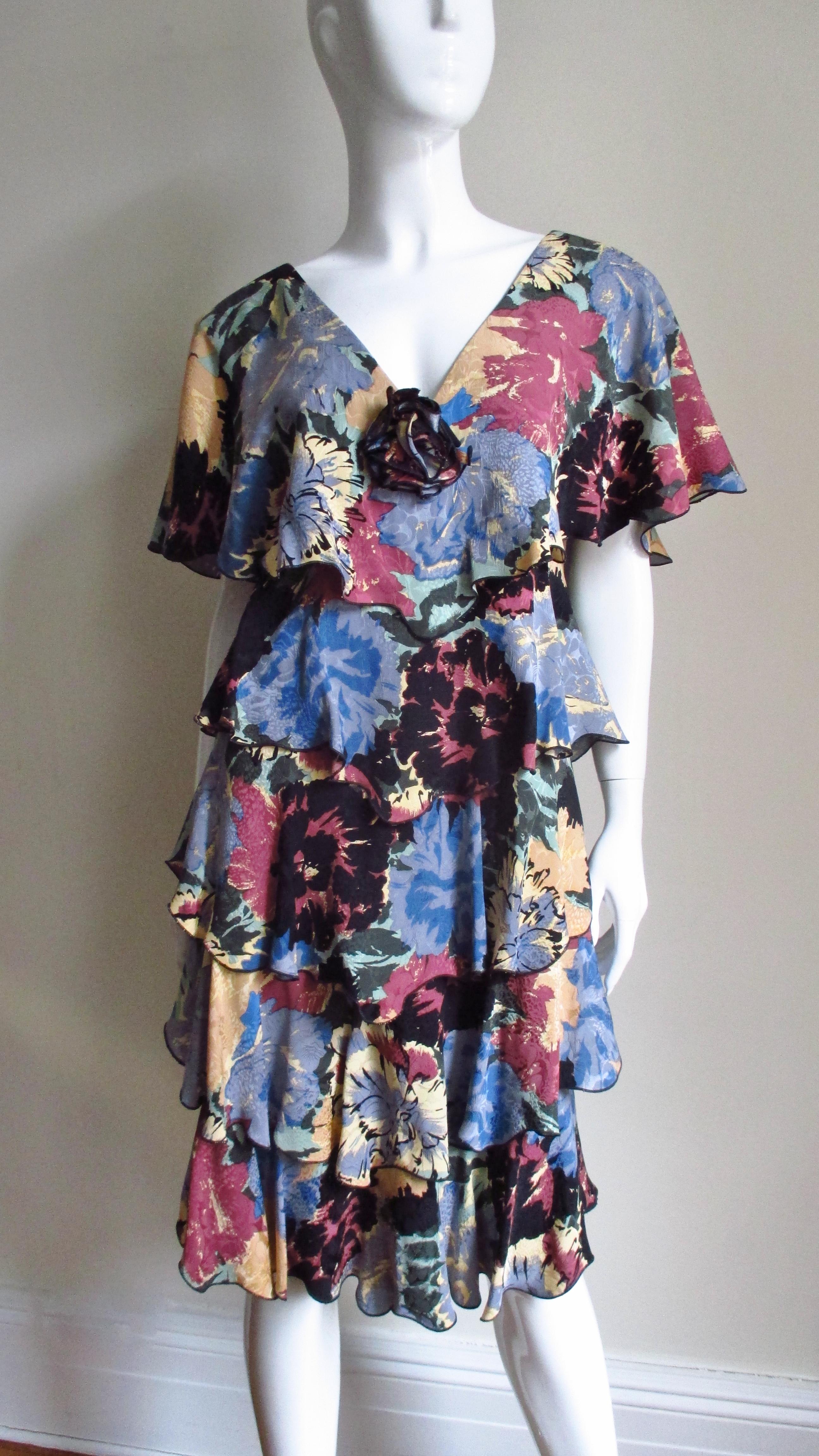 A feminine silk dress in a blue, pink, yellow and black flower pattern from notable American designer Holly Harp.  It has a V neckline front and back with 5 ruffles draping horizontally around the circumference of the dress from shoulders to the