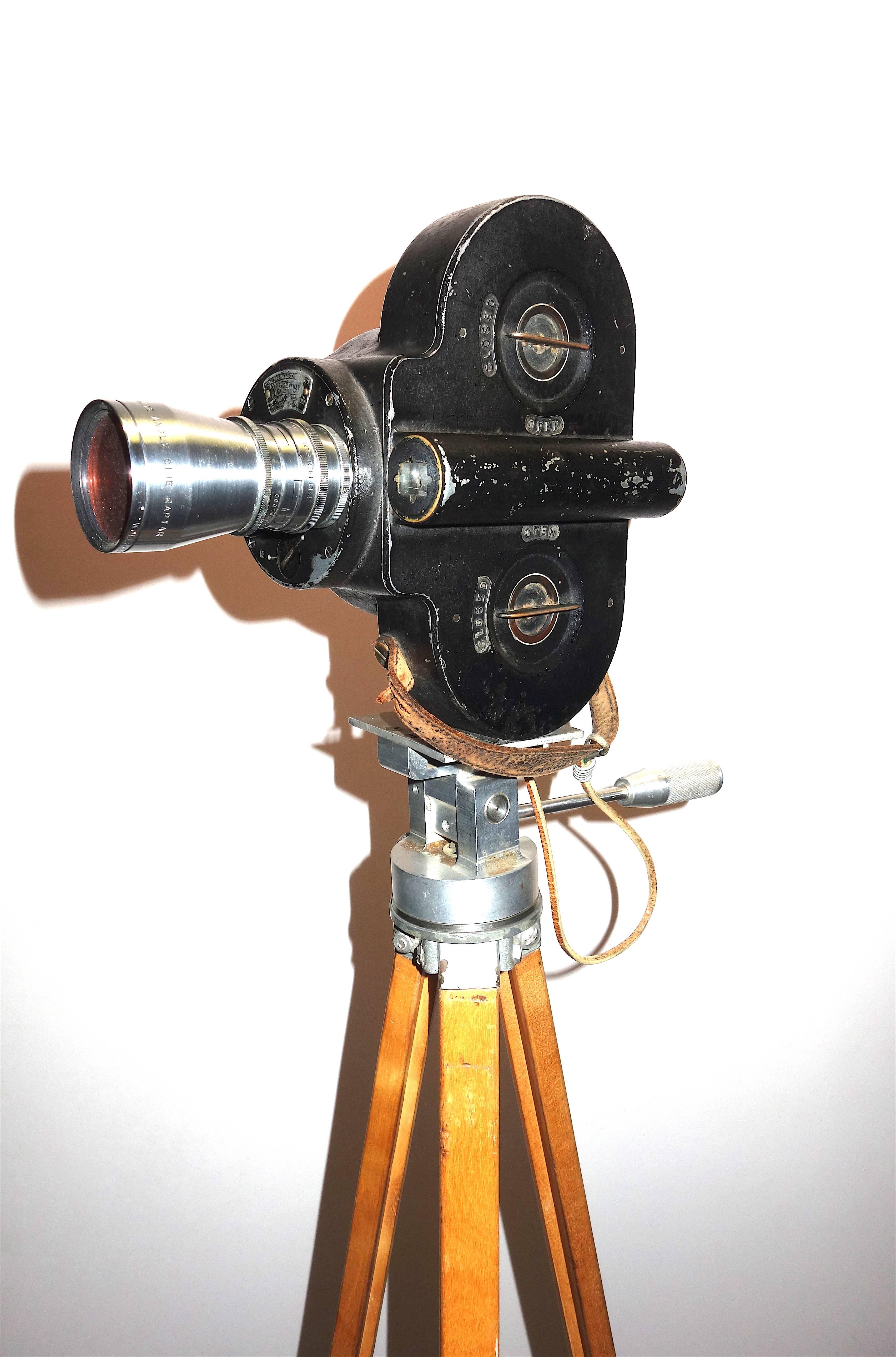 Offered for your approval is this early 20th century USA made Bell & Howell 16mm Motion Picture Camera displayed on vintage wood tripod legs.

This is an outstanding example of a 16mm professional camera with lens and early winding key sitting on a