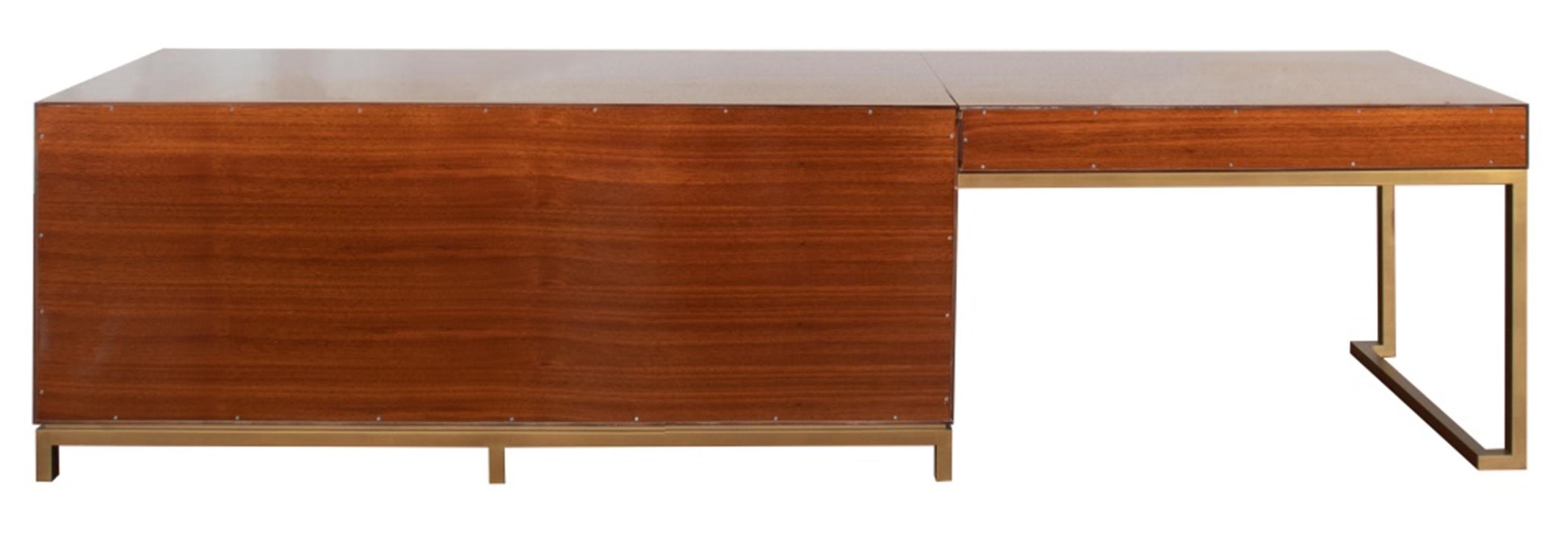 Hollywood Glam dresser vanity table, apparently unsigned, comprising a two-drawer left-facing vanity, the surface resting on a brushed brass base and single leg, with mahogany top, sides, and back, the right side conjoined to a nine drawer dresser