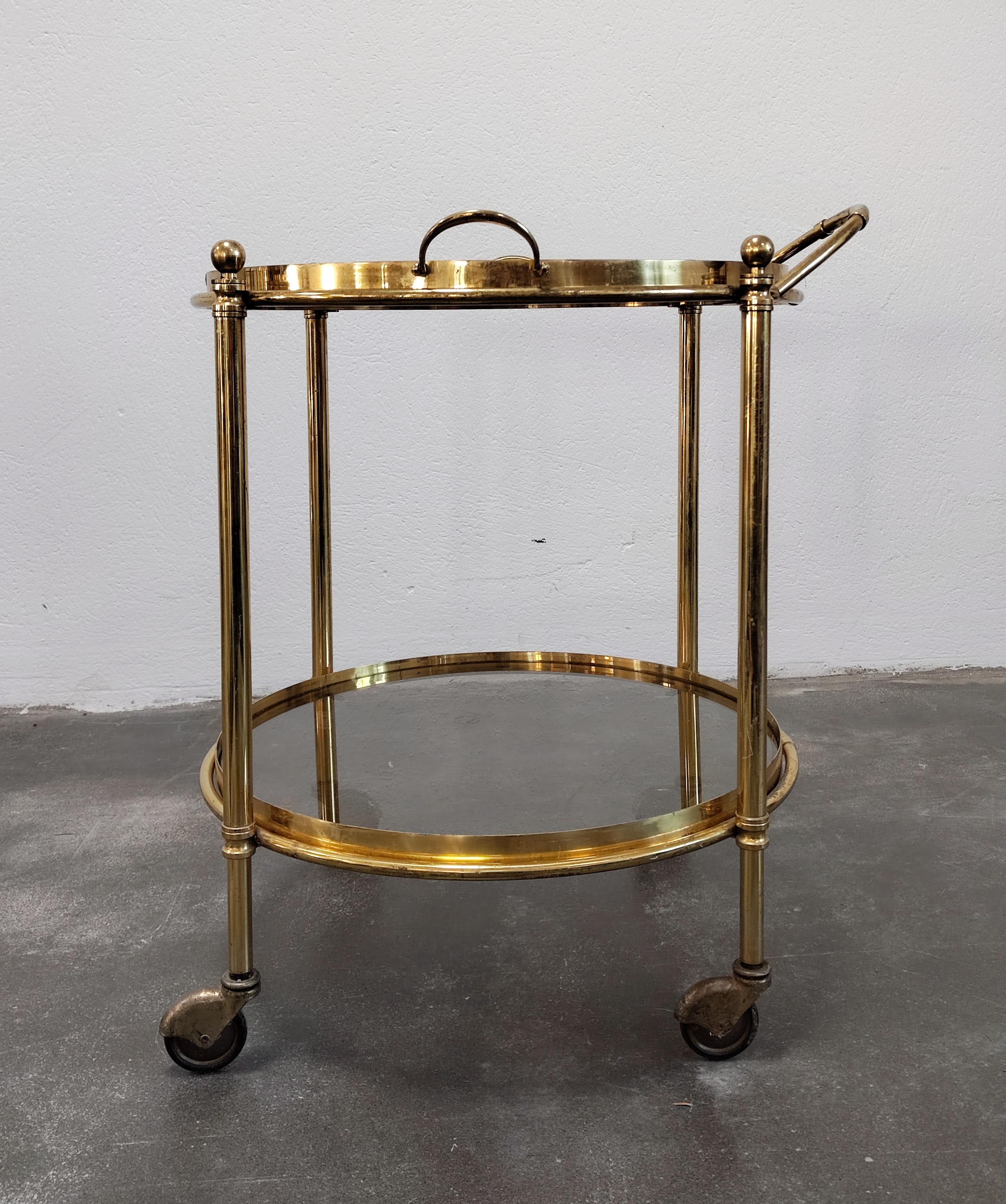 In this listing you will find a gorgeous and luxurious Hollywood Regency 2-tier bar cart done in bronze, with smoked glass boards. The top tier can be taken off and used as a serving tray, as seen in one of the pictures. Made in France in