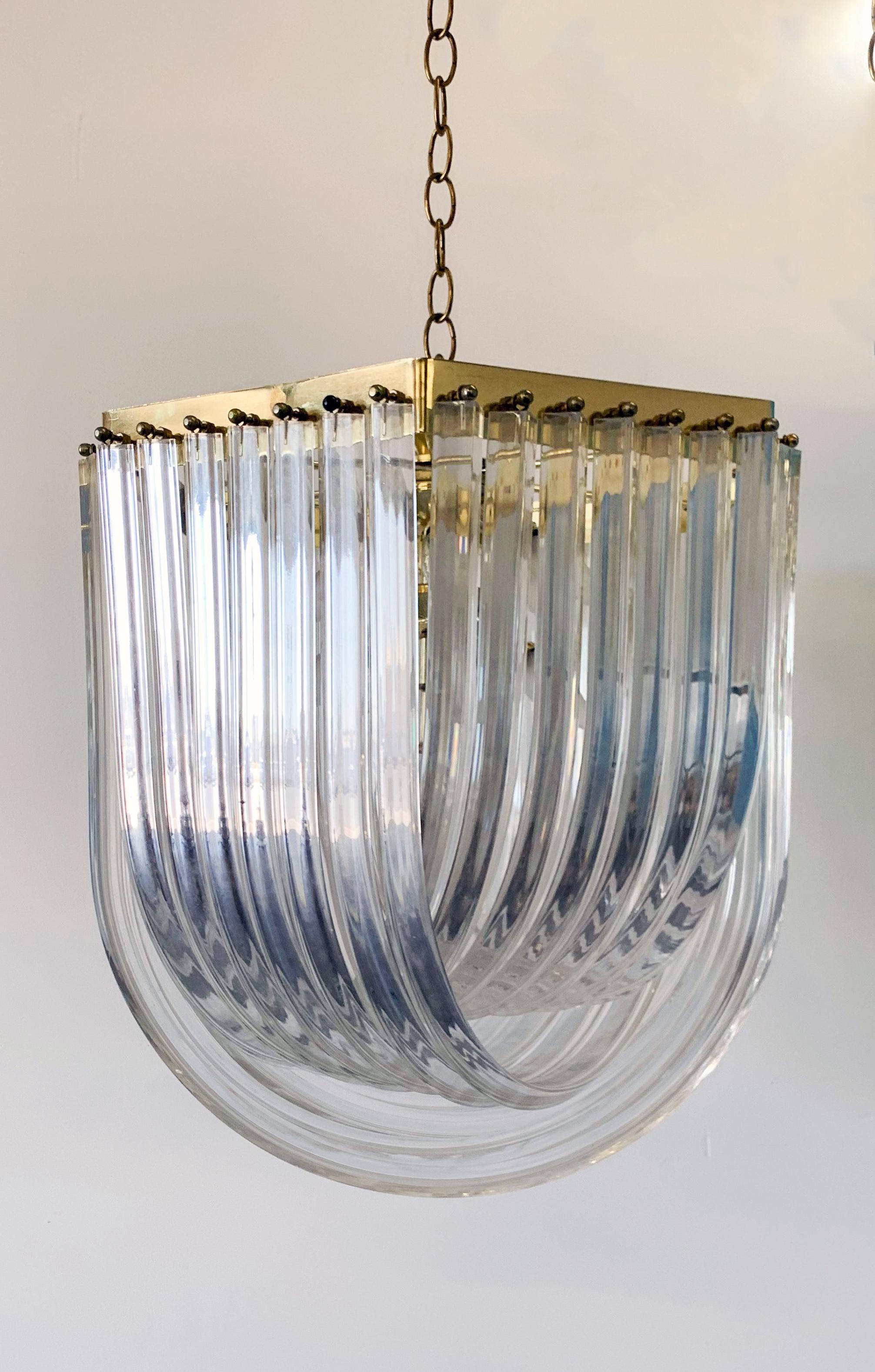 This chandelier is stunning. It features Lucite / acrylic ribbons on a brass frame with brass chain link drop cord. 

This gorgeous chandelier is in the style of Venini and would look incredible in any type of Mid-Century Modern, or Hollywood