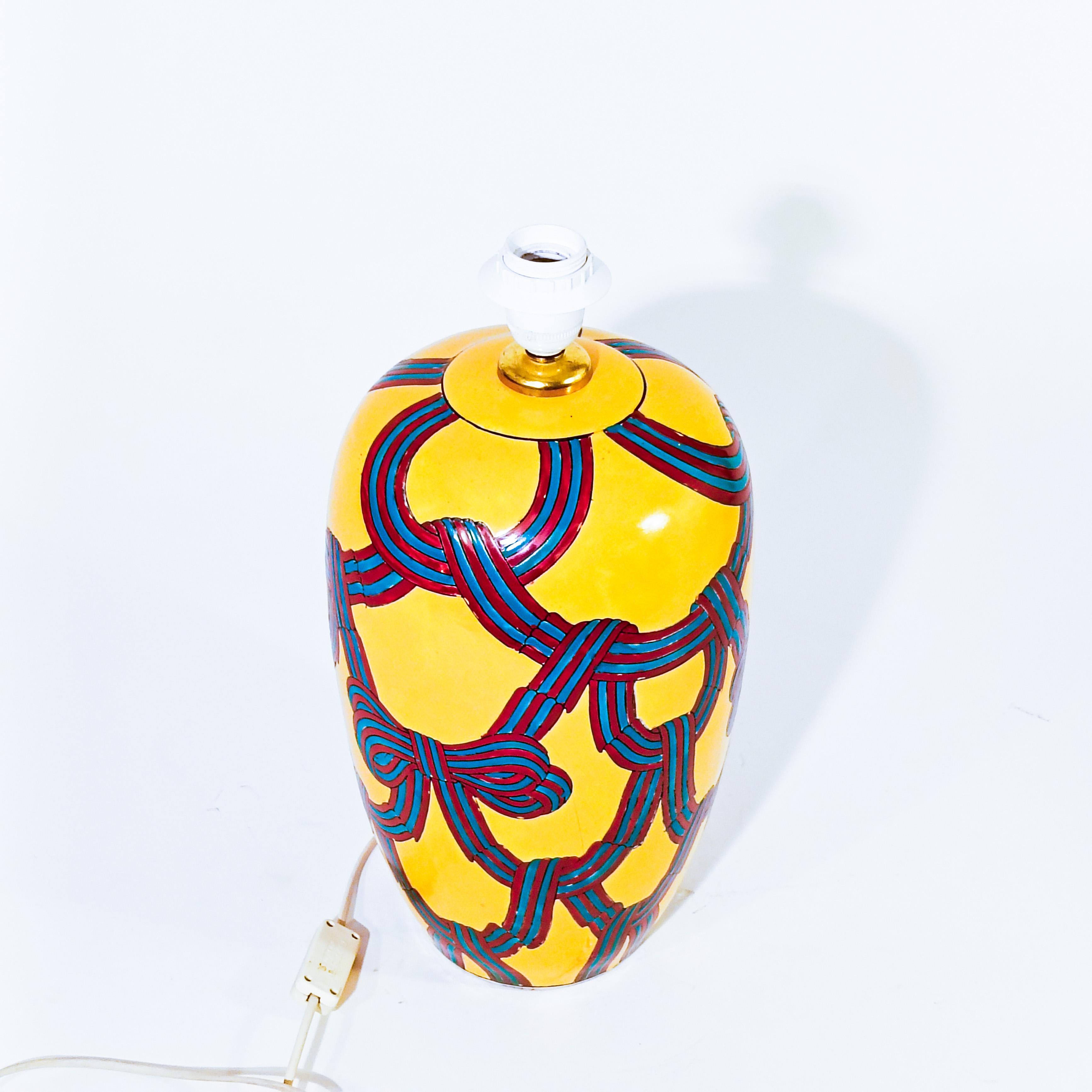 Large Hollywood Regency style ceramic table lamp, Italy, 1980s. Tibor shapped as a large hand-painted vase with striking colors. Mustard background on which a weave is arranged in the form of ribbons and bows in red and turquoise blue. Unique and
