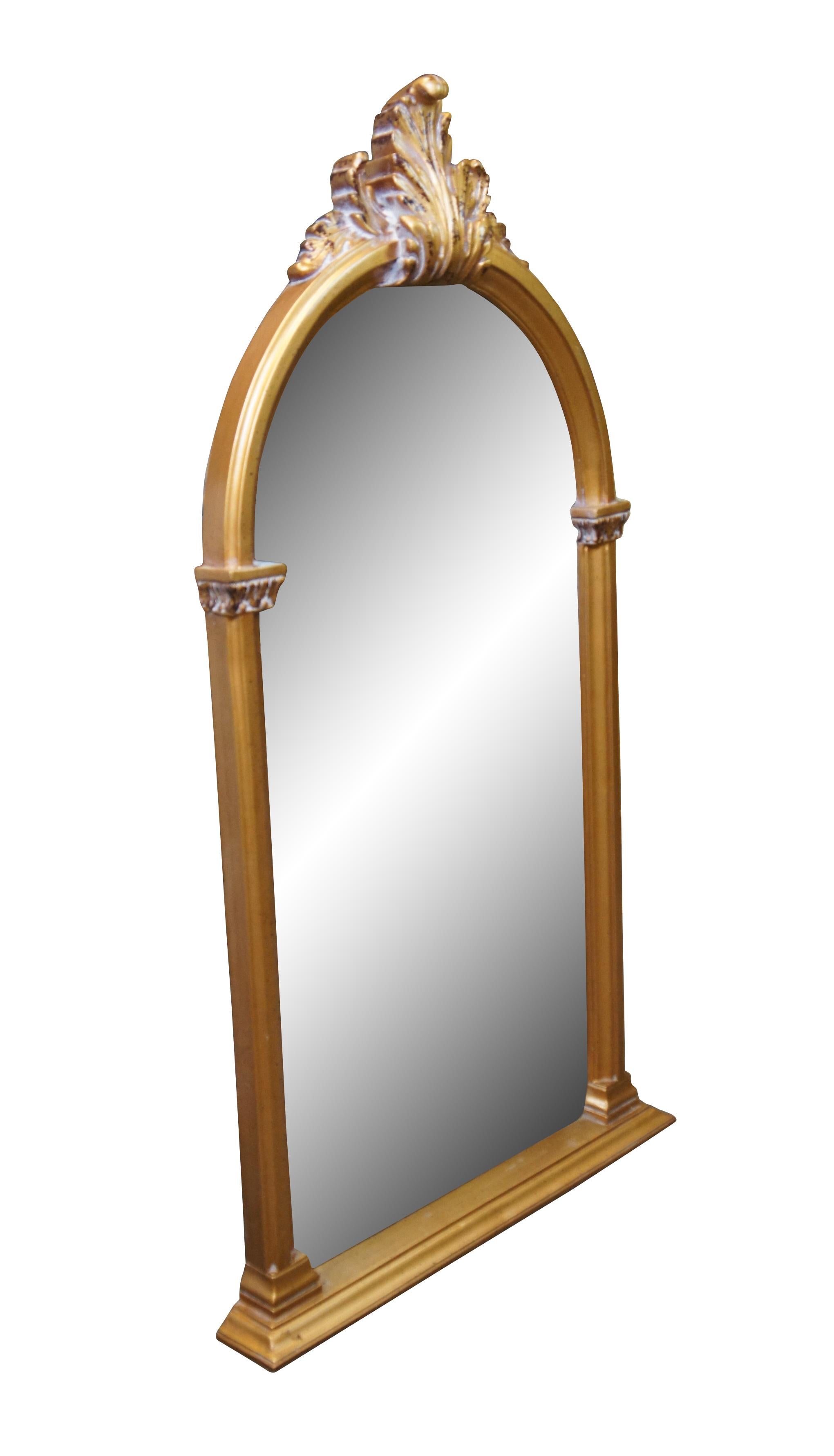 Miroir mural de style Hollywood Regency de la fin du 20e siècle, de forme arquée, flanqué d'une base à pieds, de colonnes simples surmontées de feuilles sur les côtés et d'une haute crête de feuilles d'acanthe au sommet. Peint en or brillant,