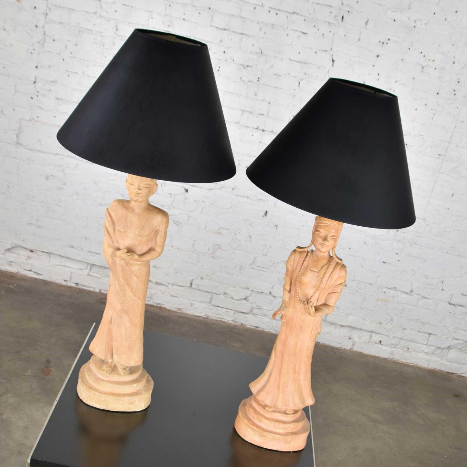 Handsome pair of Hollywood Regency Asian female and male figural lamps in the style of James Mont wearing black hard backed fabric tapered shades. They have a marking of Bodhisattva, Hilgos. They are in wonderful vintage condition. There have been