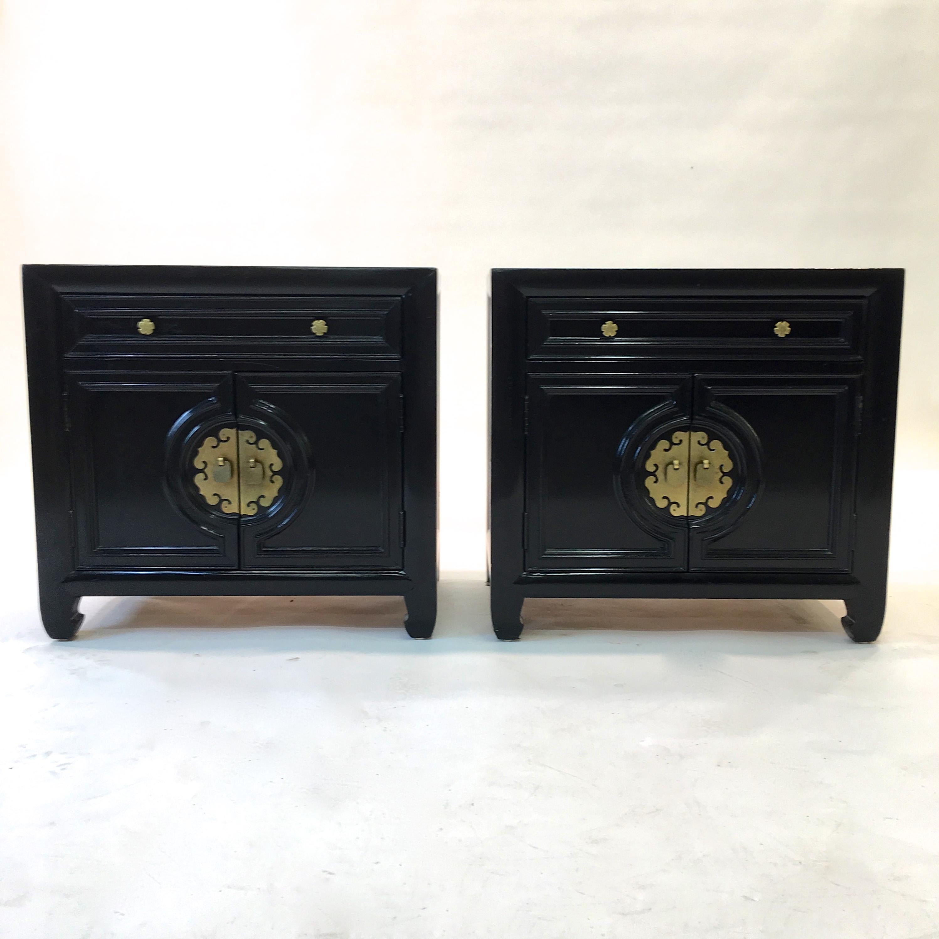 Vintage 1960s black painted pair of nightstands by Century Furniture with solid brass hardware and central oriental motif brass medallion. Two double doors below a single drawer with Century brand mark. The doors open to reveal an open compartment.
