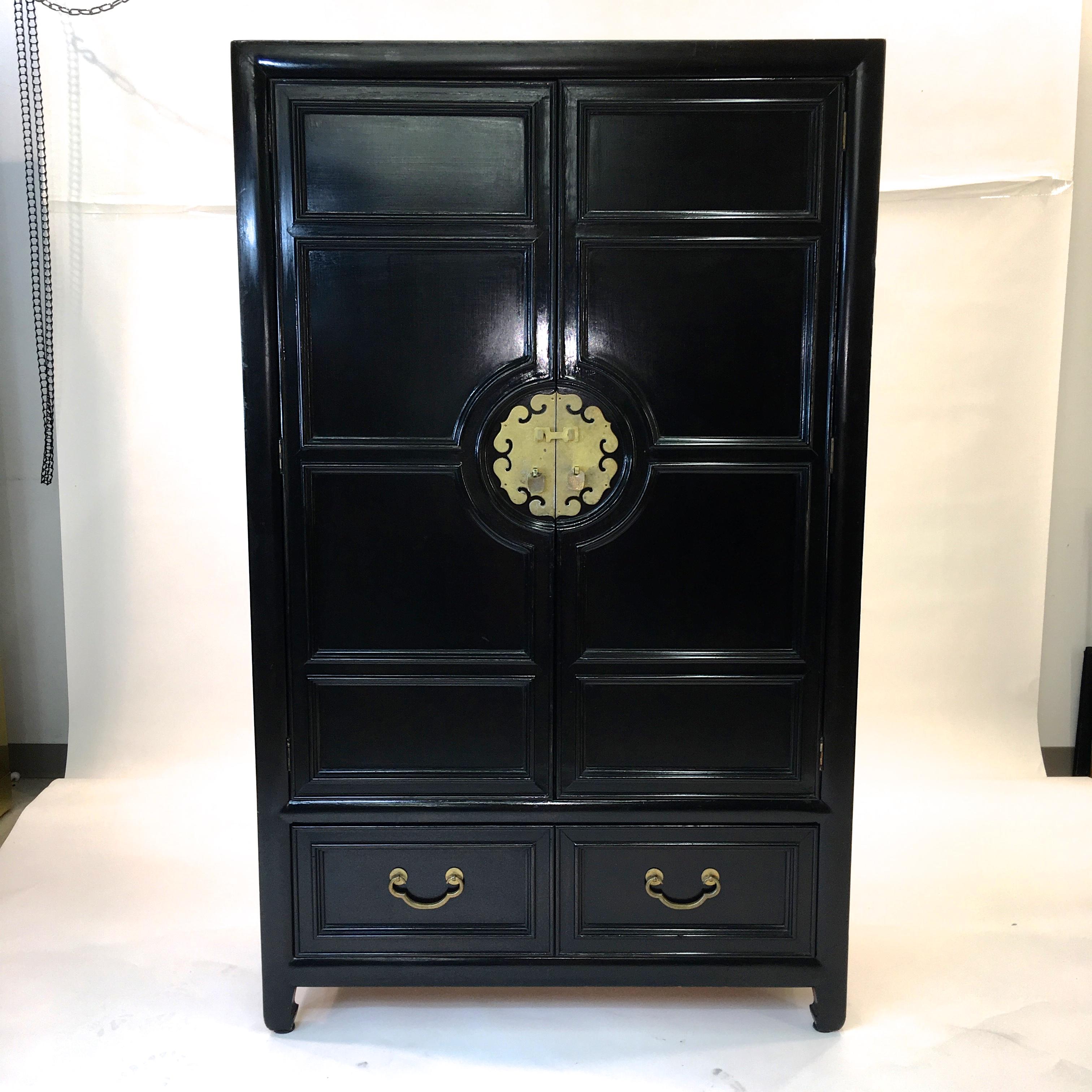 Vintage 1960s black painted wardrobe chest of drawers by Century Furniture with solid brass hardware and central oriental motif brass medallion. Two large double doors above a single drawer. The doors open to reveal an open shelf, a divided open