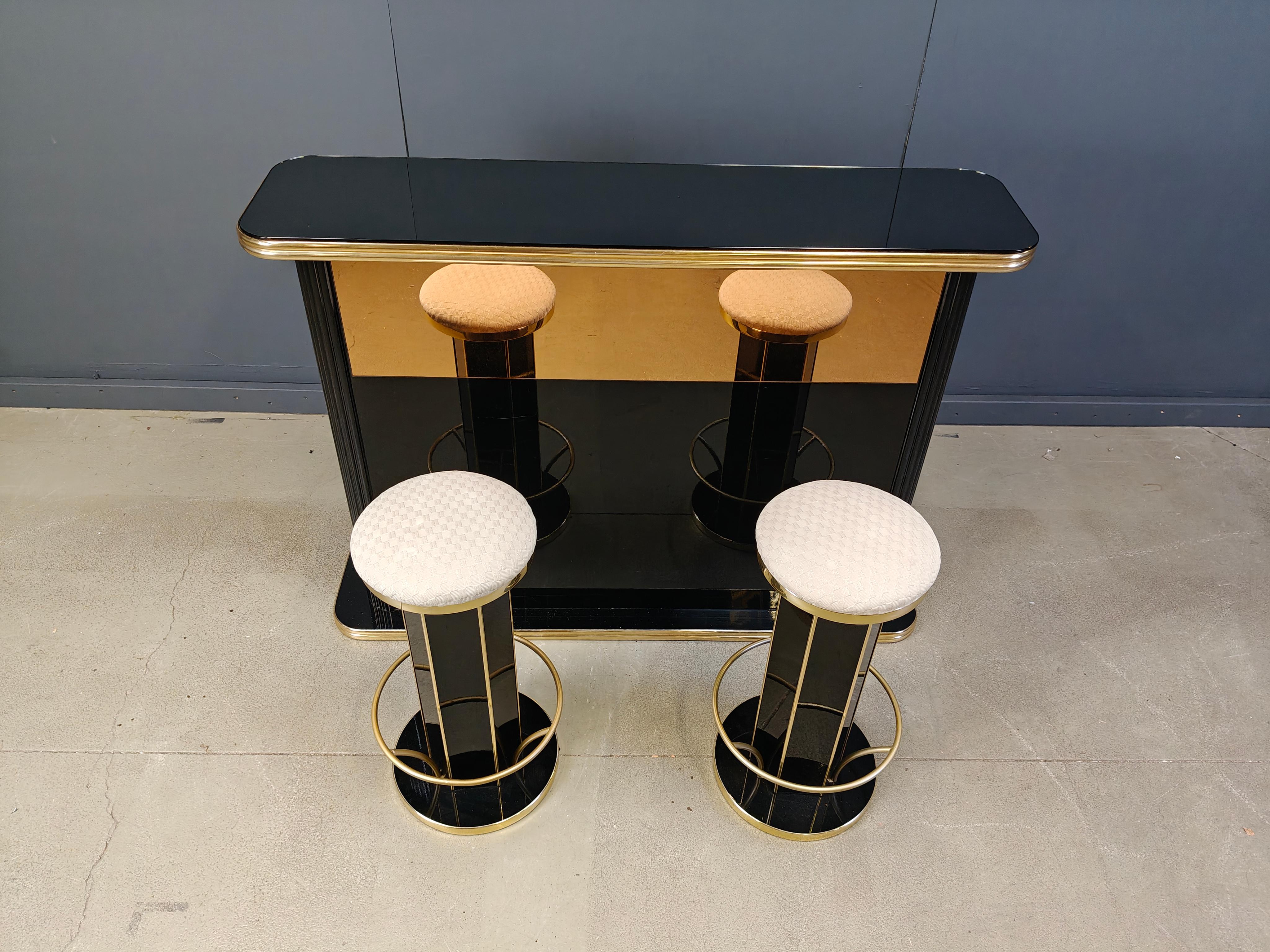 Vintage dry bar with two bar stools made from lacquered wood and brass.

The bar has a mirrored glass at the front and a shelve inside and a black glass top.

Great eye catcher to welcome your guests in a luxury/seventies glam fashion.

1970s -