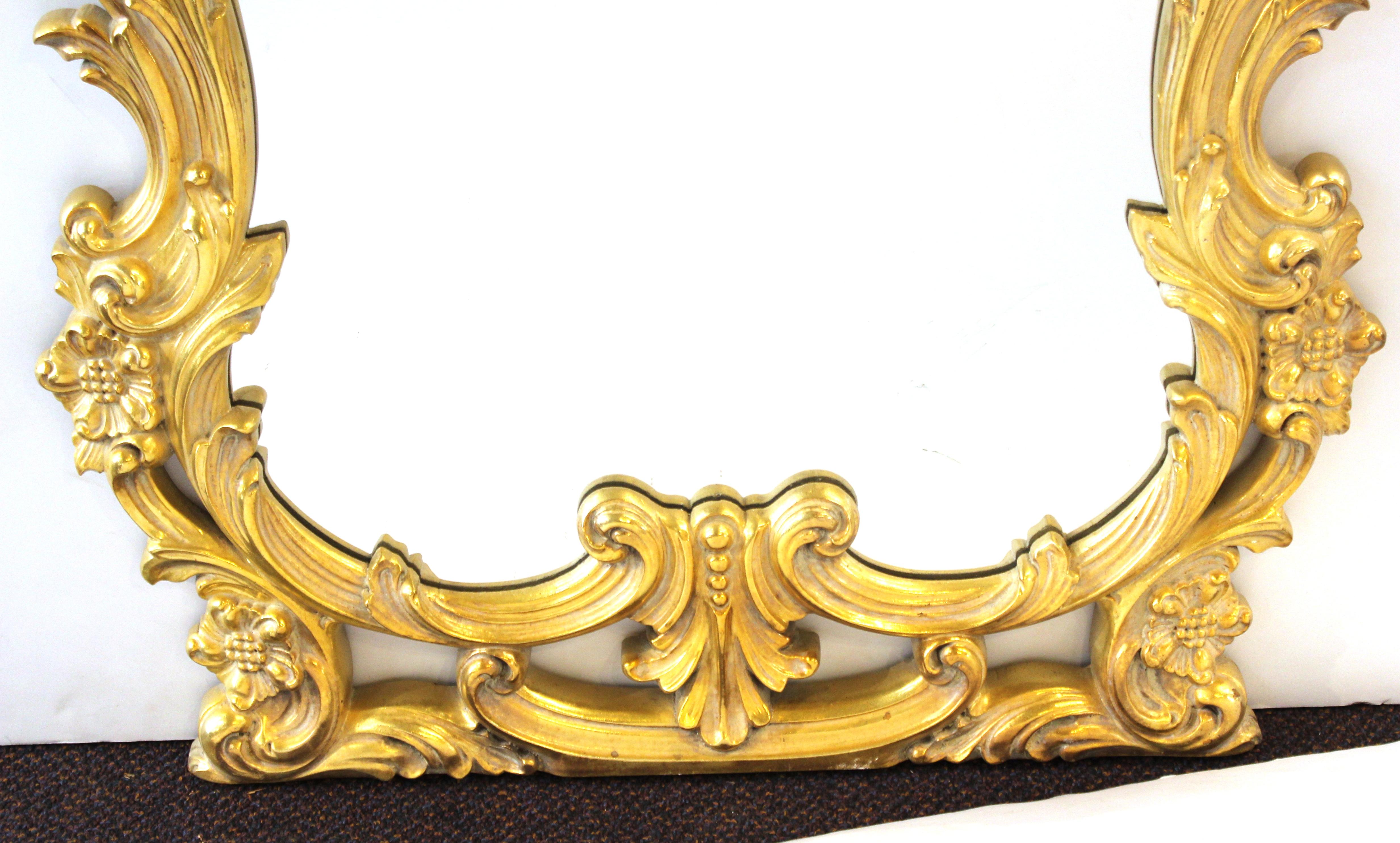 Hollywood Regency Baroque revival style wall mirror with elaborate gold frame. The piece was made in the late 20th century and is in great vintage condition with age-appropriate wear.