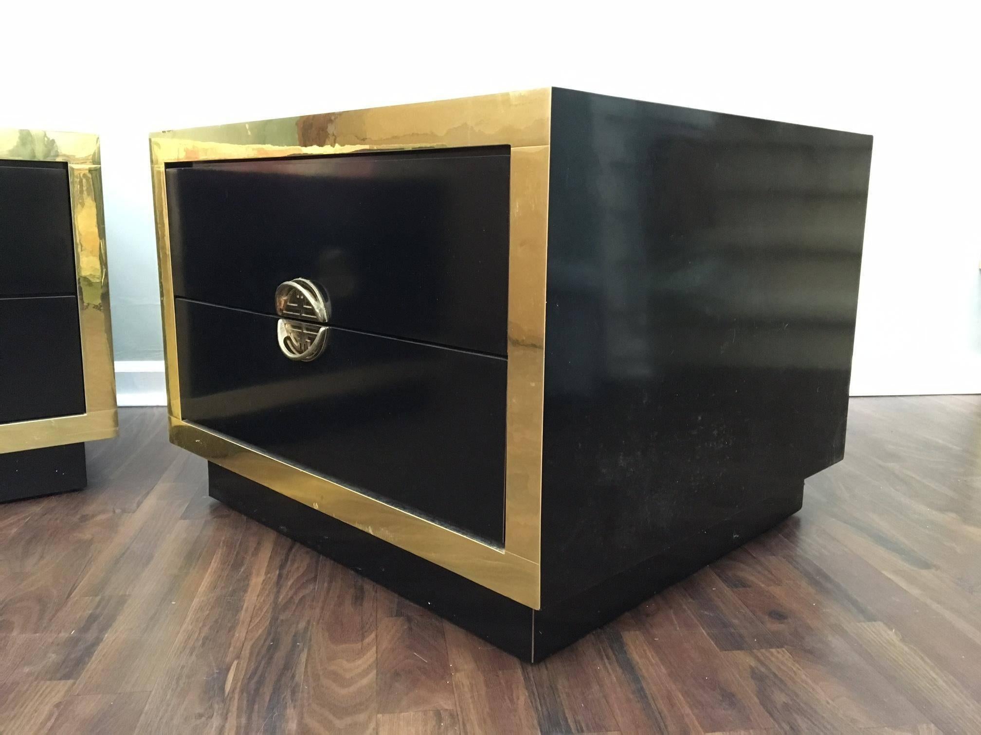 Black and gold Hollywood Regency nightstands feature Asian chinoiserie brass hardware and mirror finish. Each has two drawers and are in excellent vintage condition other than chip on lower rear side and small dent on top rear corner (see photos).