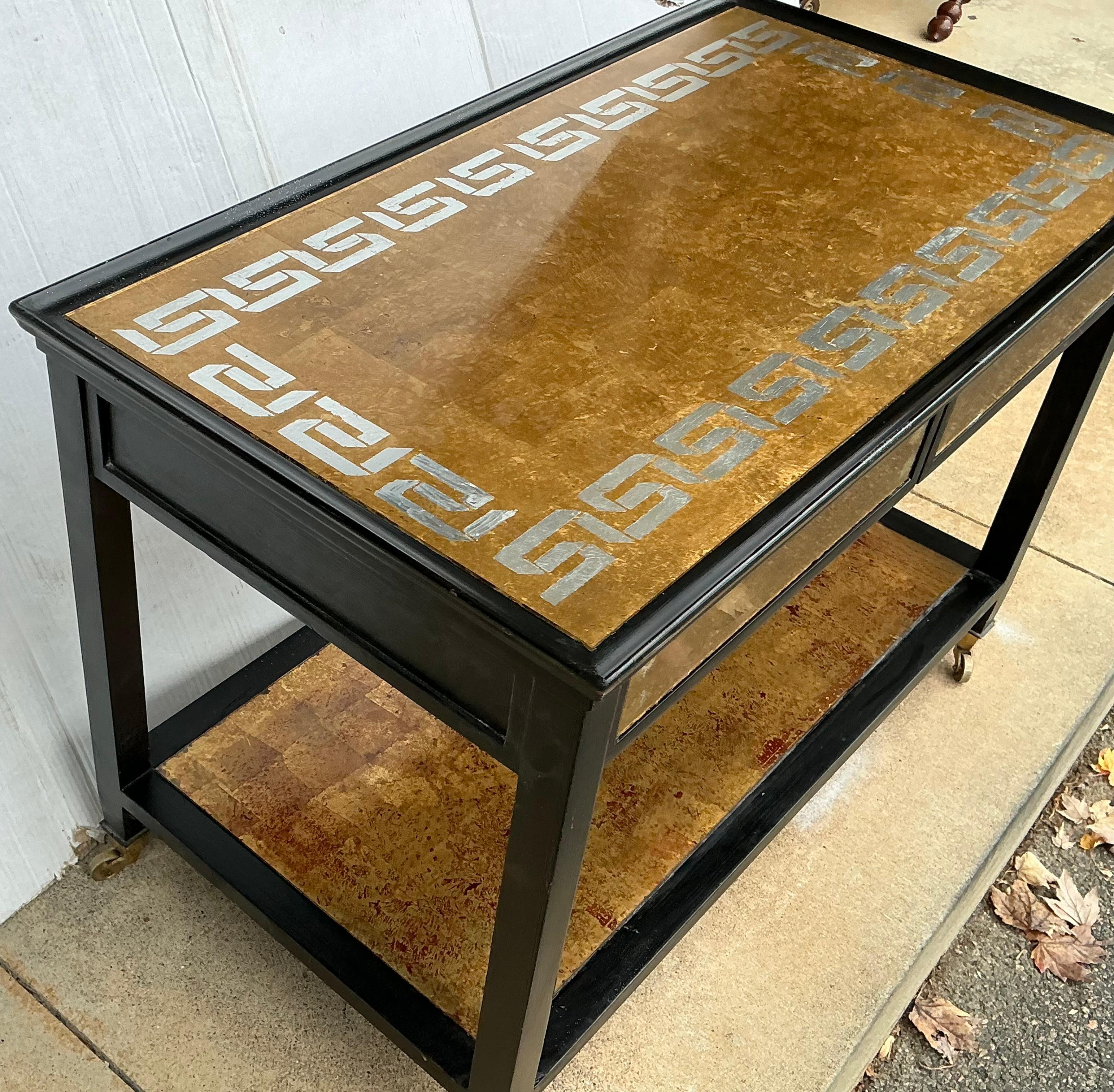 This is a striking pair of Italian Hollywood Regency gilt and black side tables with two drawers over a single tier. The tops are reverse painted gilt glass with silver Greek Key border. The bottom glass shelf is the same but without the Greek Key.