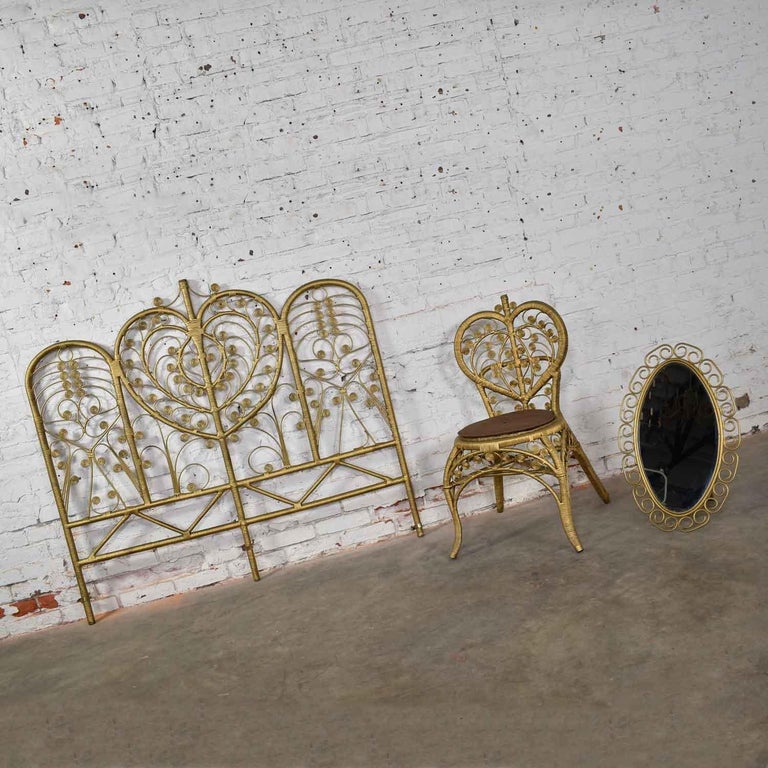 Glorious Hollywood Regency Bohemian bedroom trio comprised of a full-size gold wicker scroll headboard, a heart backed gold wicker chair, and a scrolled gold wicker mirror. They are all in wonderful vintage condition with no outstanding flaws we